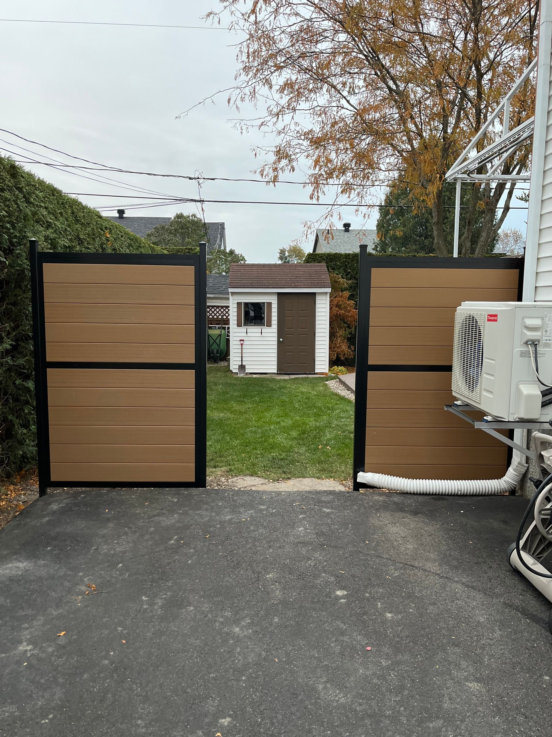 Un portail en bois est ouvert sur une allée avec un hangar en arrière-plan.