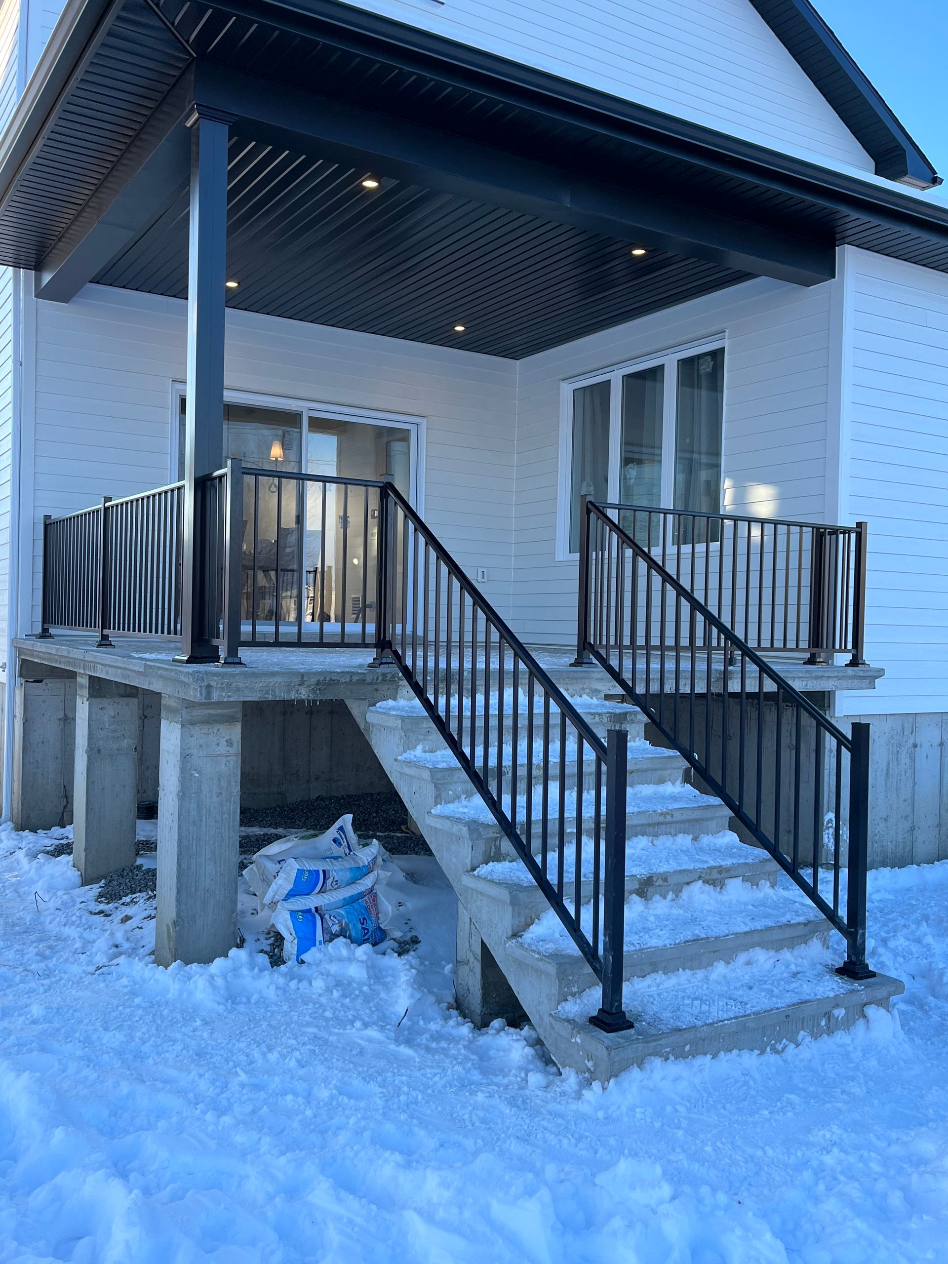 Une maison blanche avec une balustrade noire et des escaliers dans la neige.