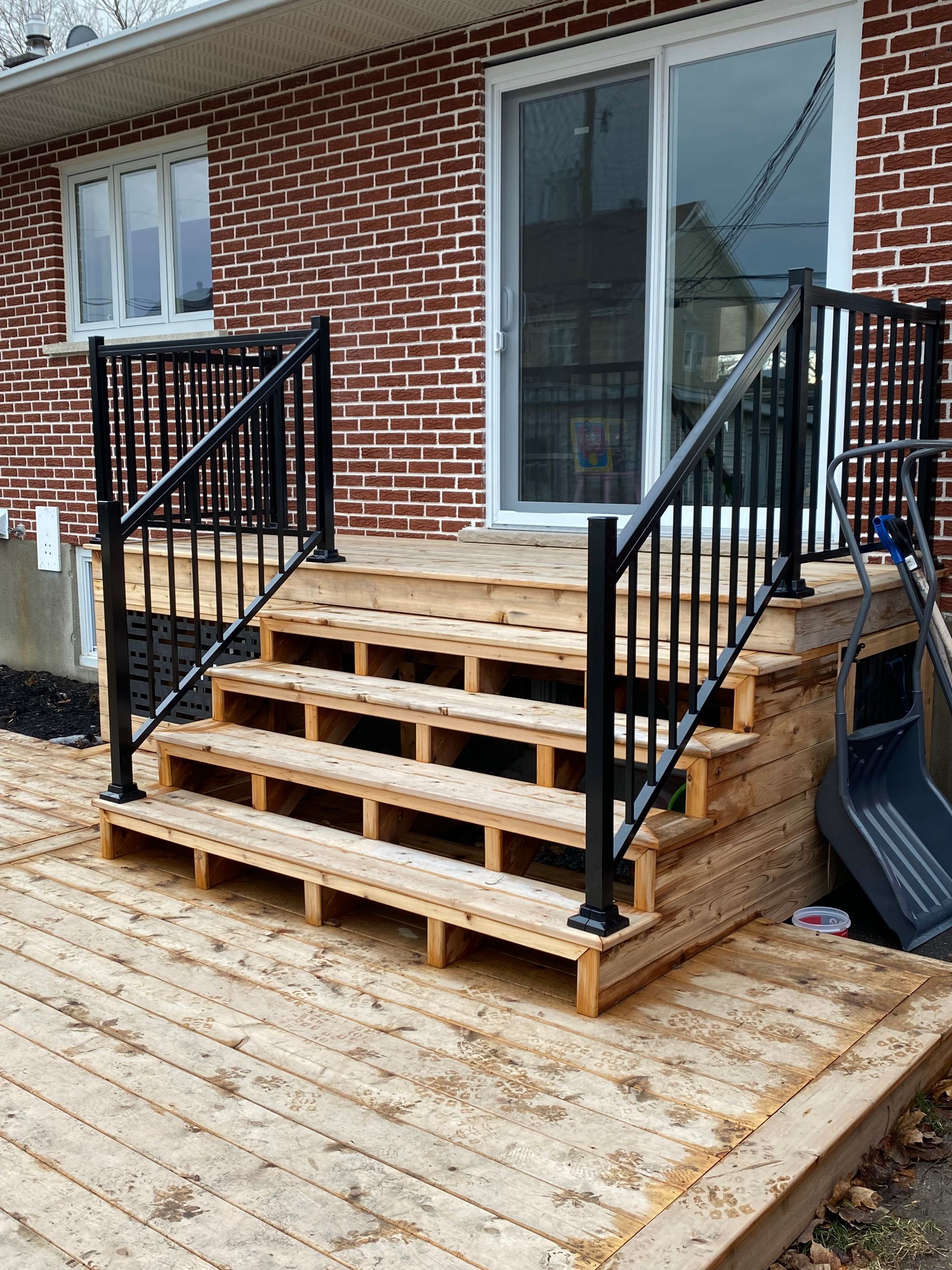 Une terrasse en bois avec des escaliers et une balustrade en métal devant une maison en brique.
