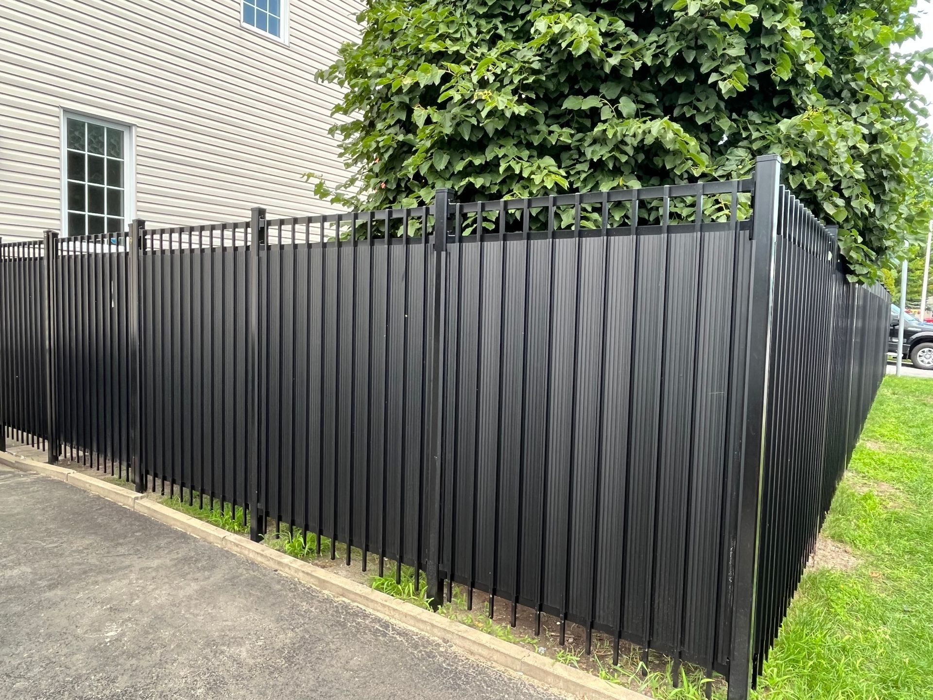 Une clôture noire avec un arbre en arrière-plan se trouve devant une maison.