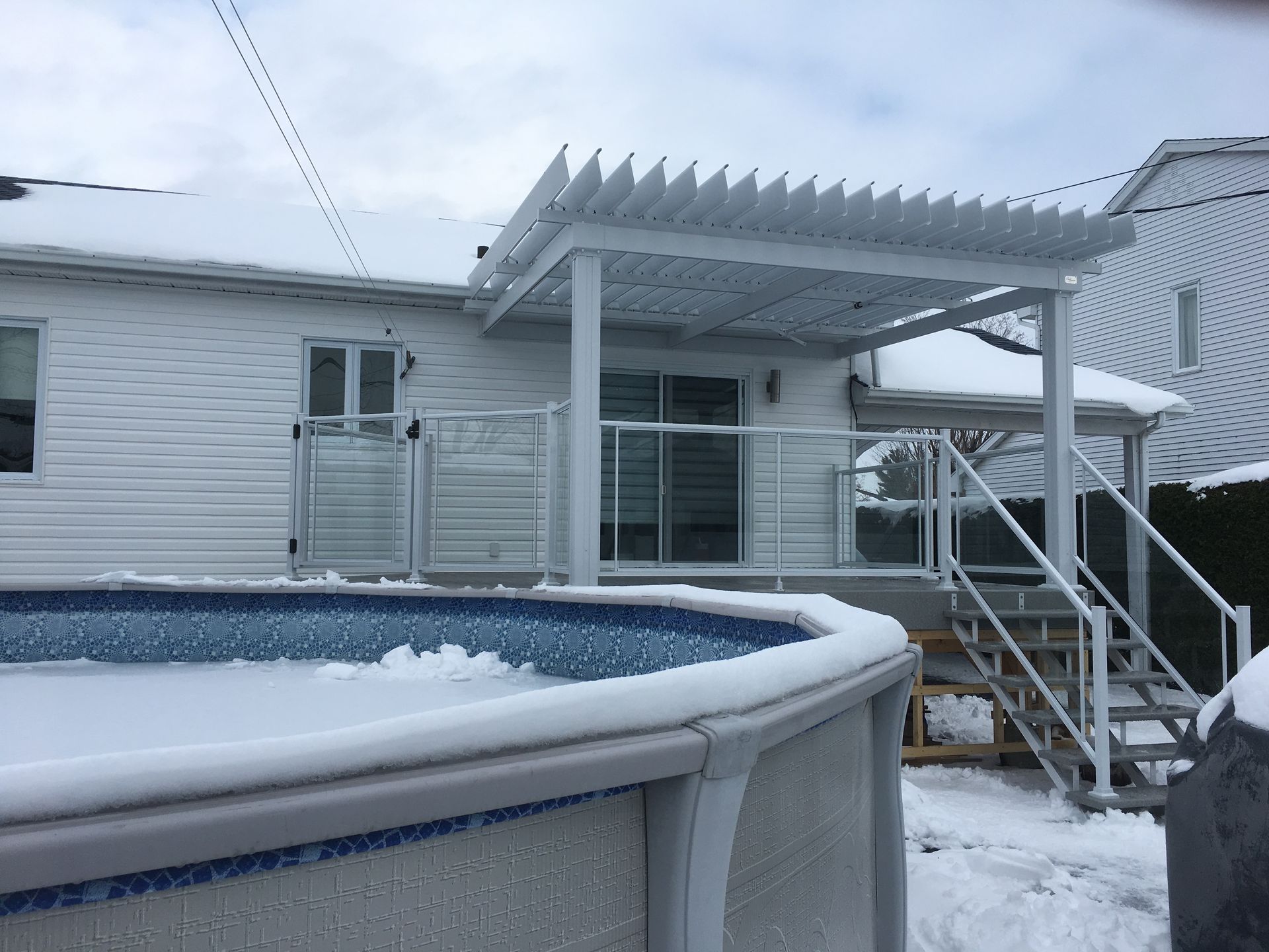 Une piscine est recouverte de neige devant une maison.