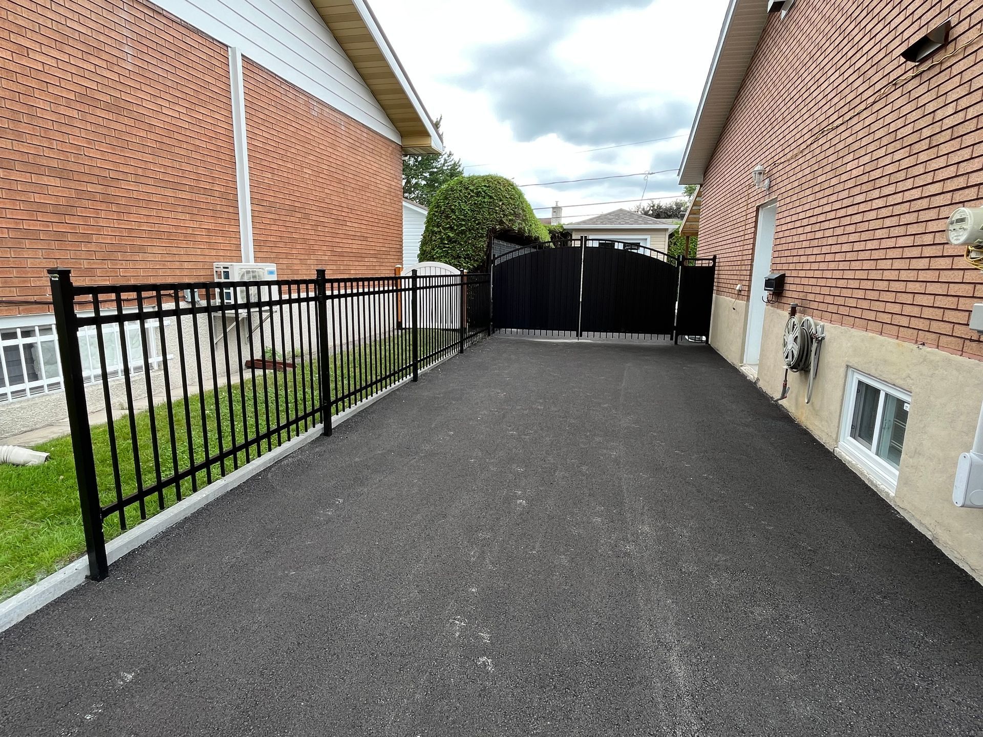 Une allée menant à une maison en brique avec une clôture en métal.