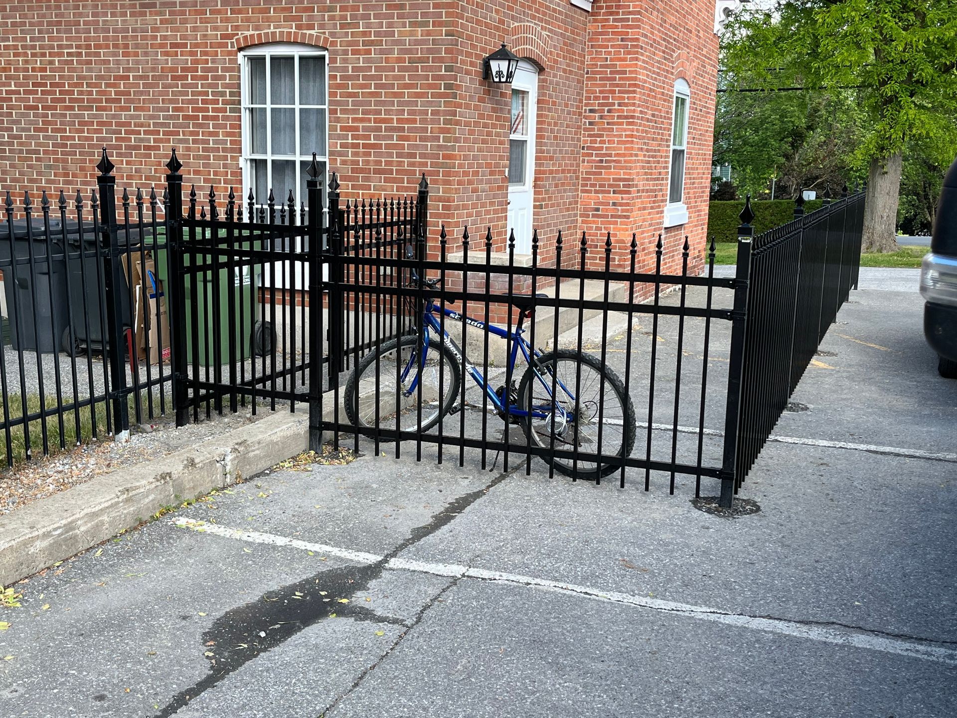 Un vélo est enchaîné à une clôture noire devant un bâtiment en briques