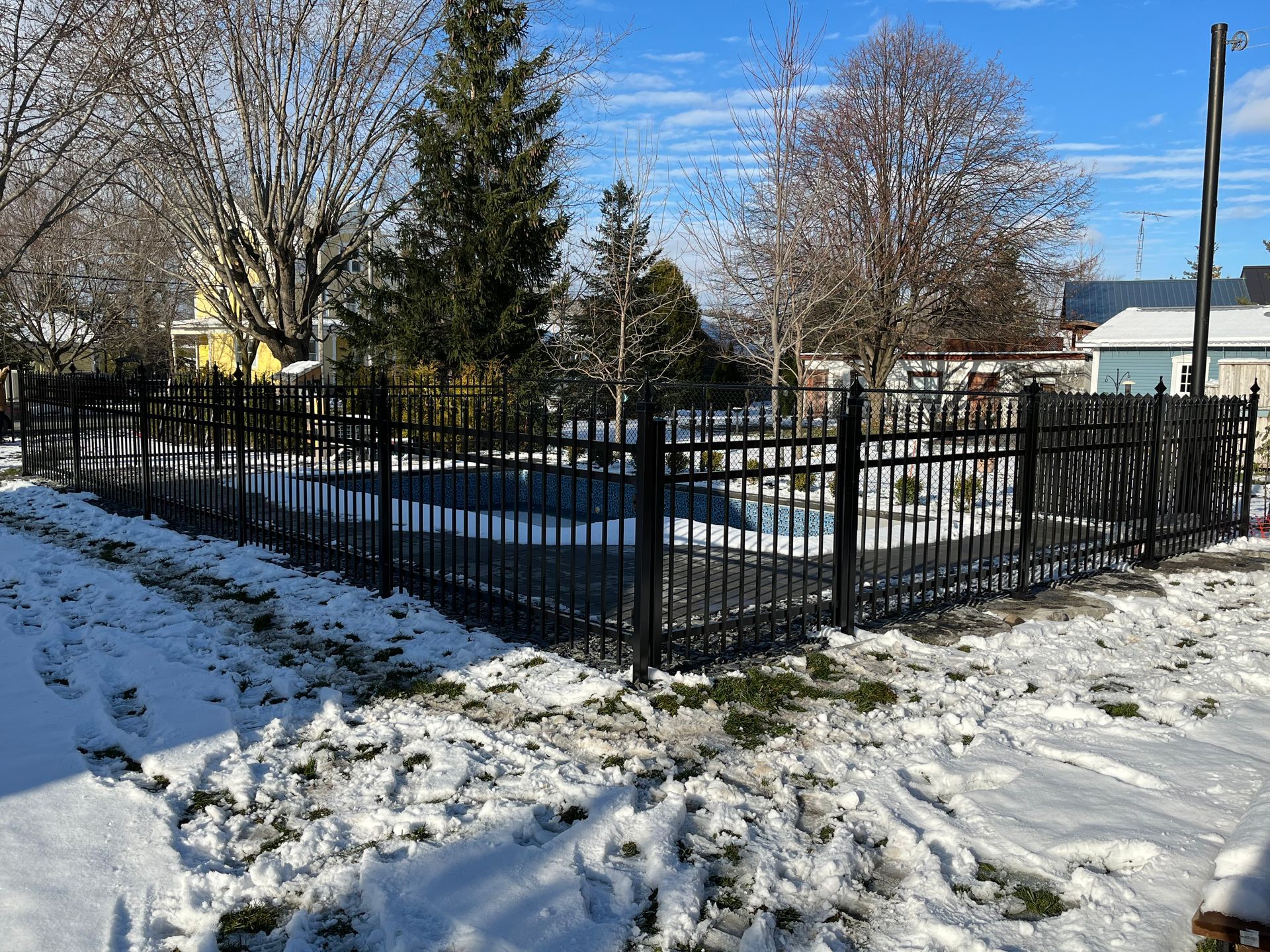 Une clôture noire entoure une piscine sous la neige.