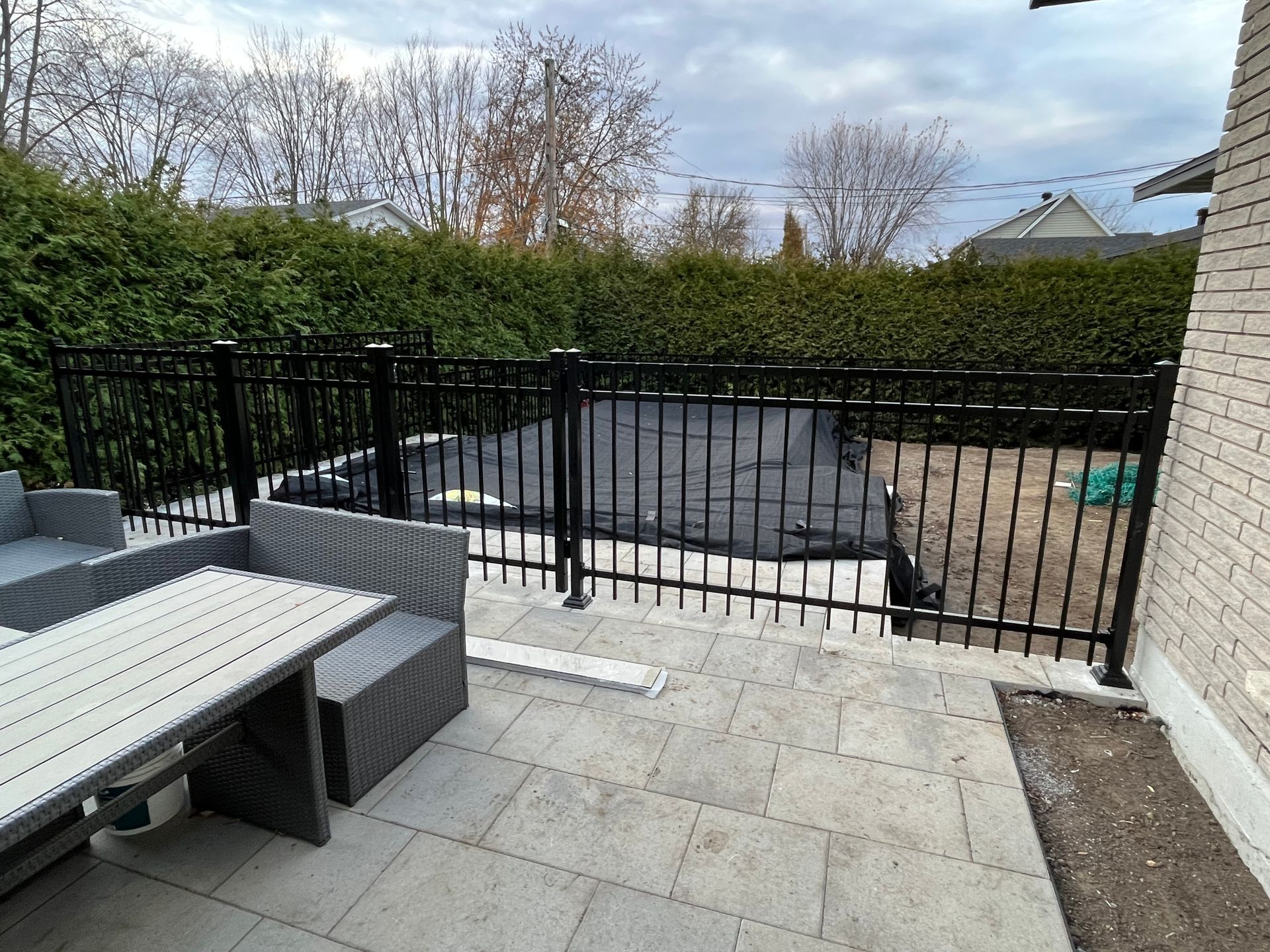 Une clôture noire entoure un patio avec une table et des chaises.