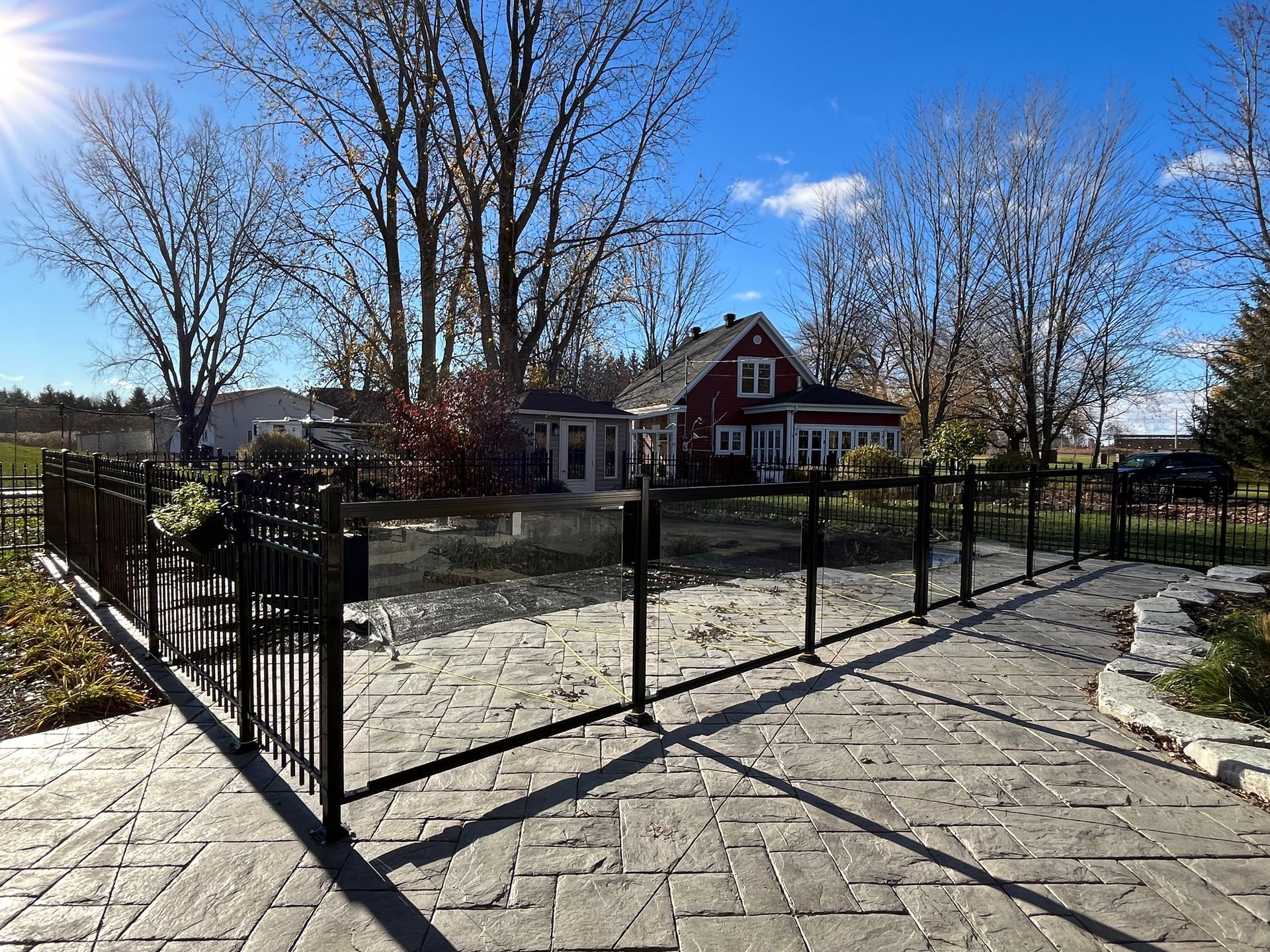 Une clôture entoure un patio avec une maison rouge en arrière-plan.