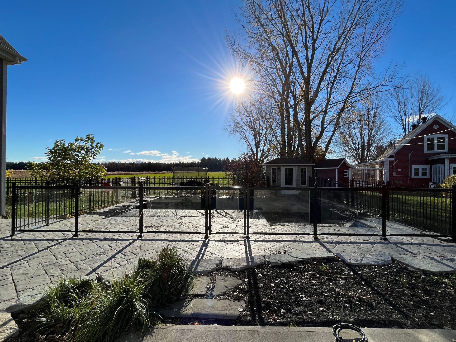 Le soleil brille fort sur une cour clôturée avec une grange rouge en arrière-plan.