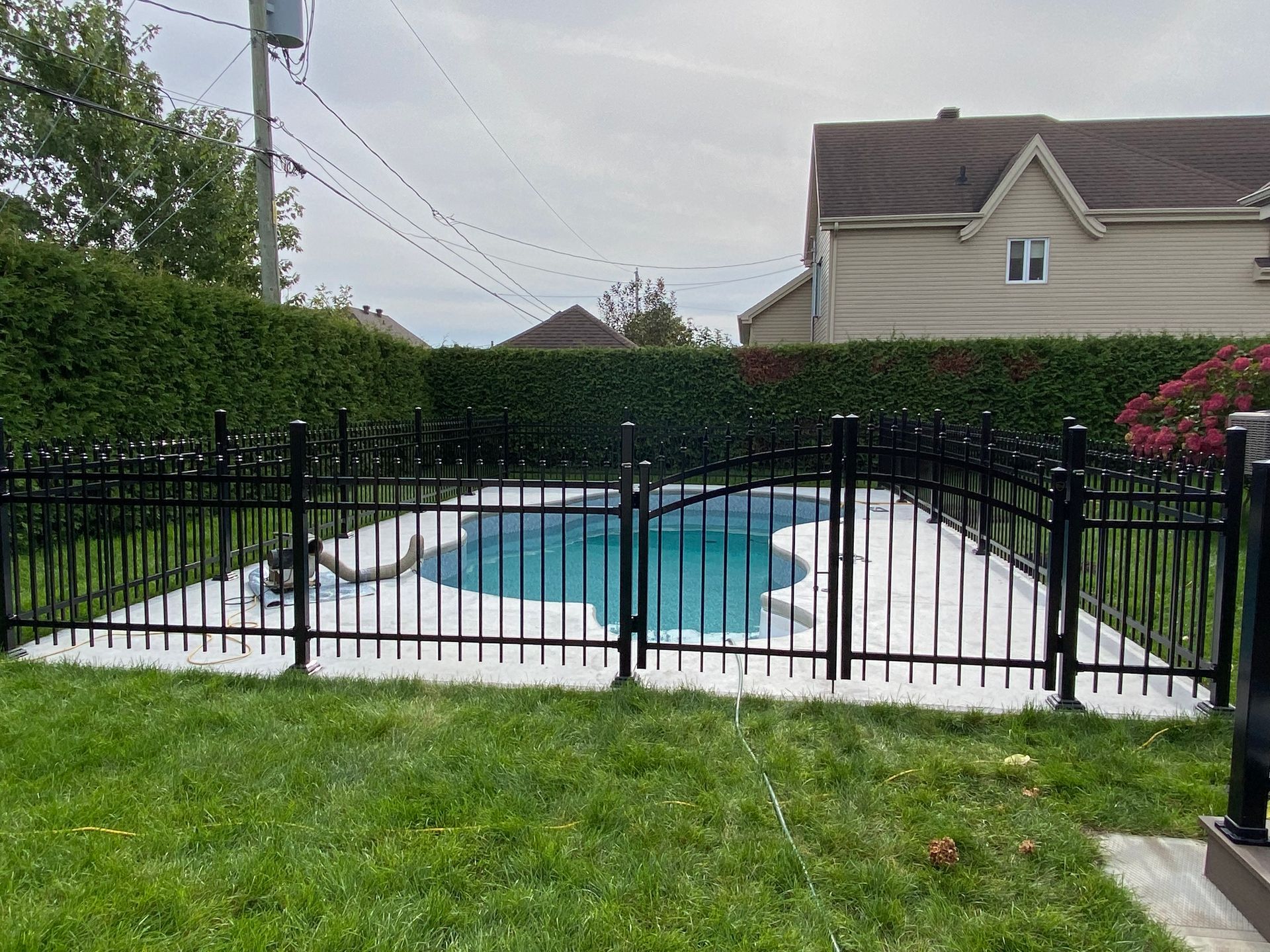 Une clôture noire entoure une piscine dans une cour arrière.