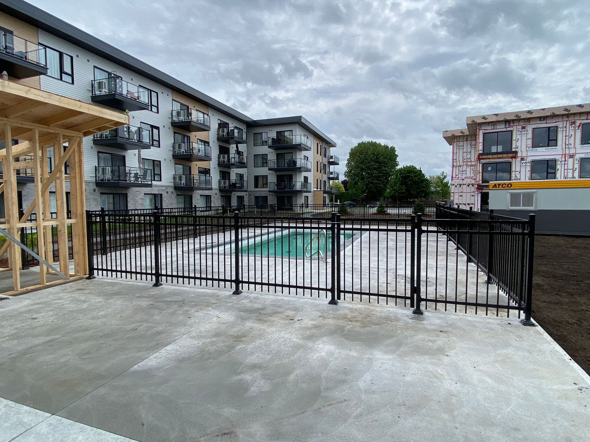 Une clôture entoure une piscine devant un immeuble en construction.