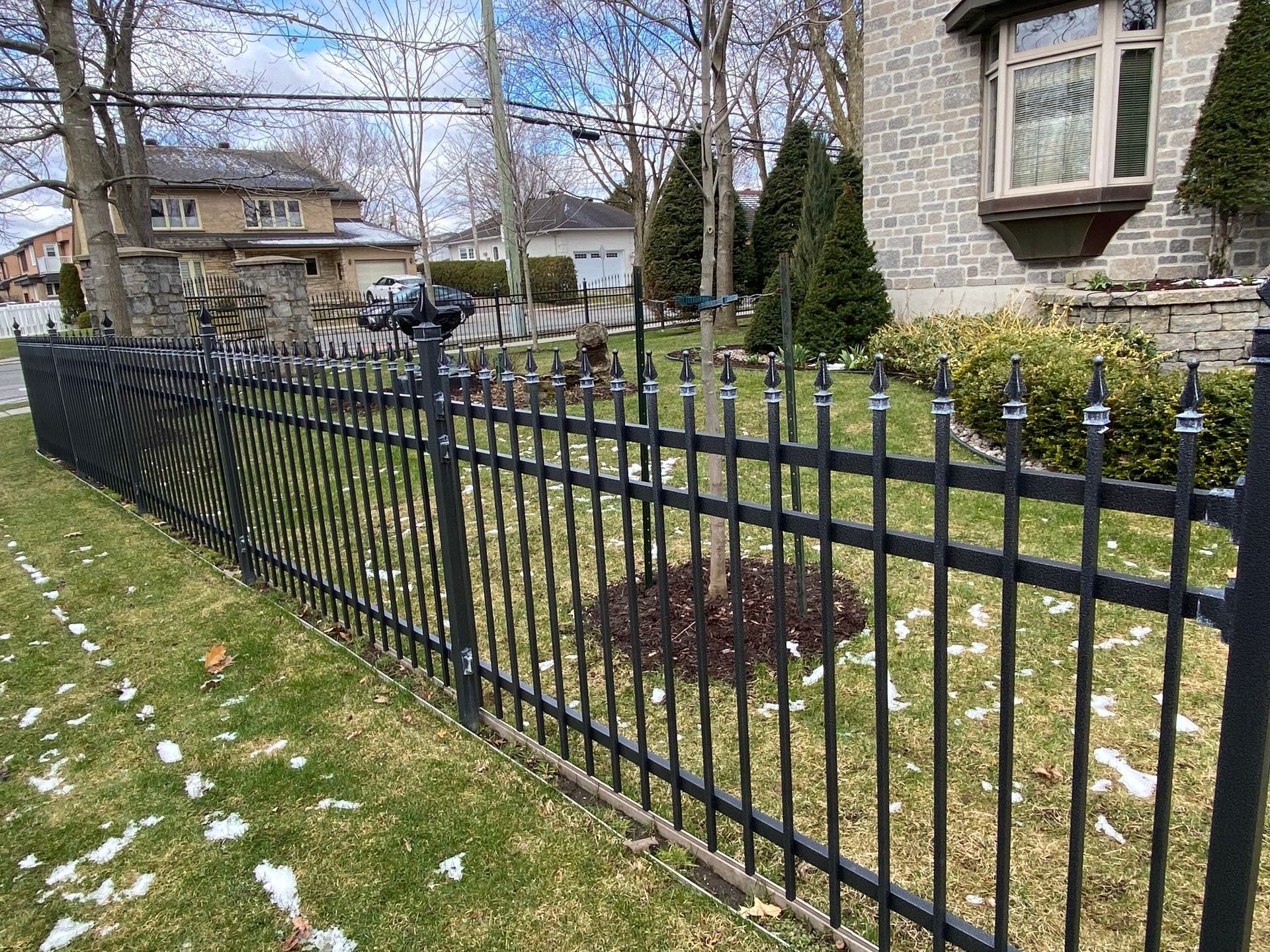 Une clôture en métal noir entoure une cour verte luxuriante devant une maison.