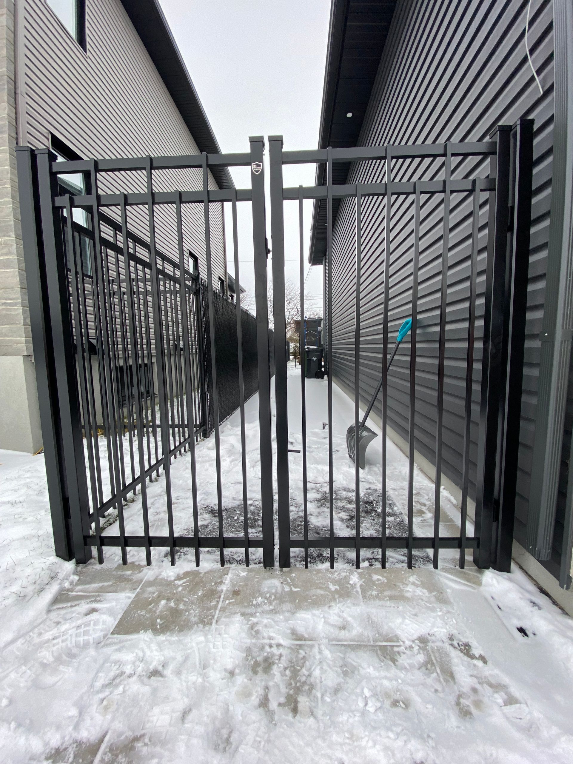 Un portail noir est assis dans la neige à côté d'une maison.