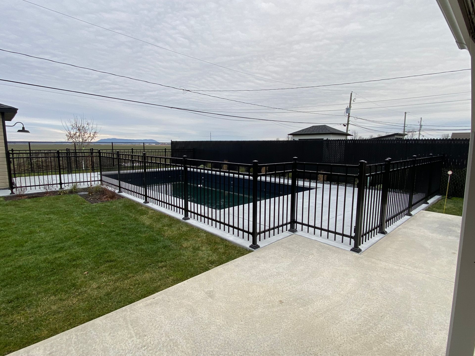 Une clôture noire entoure une piscine dans une cour arrière.