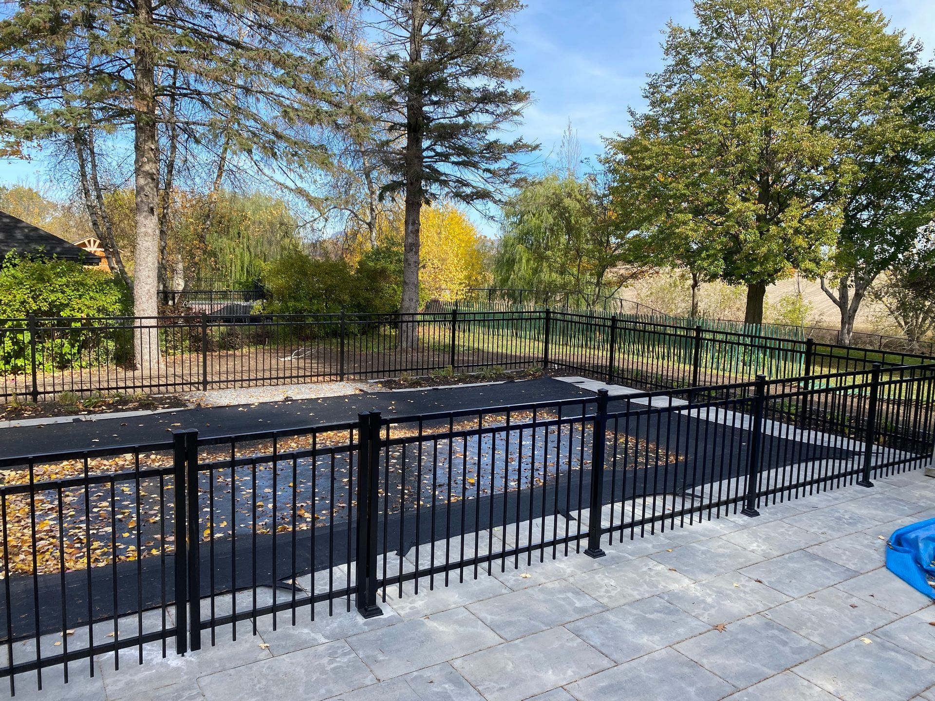 Une clôture noire entoure une piscine avec des arbres en arrière-plan.