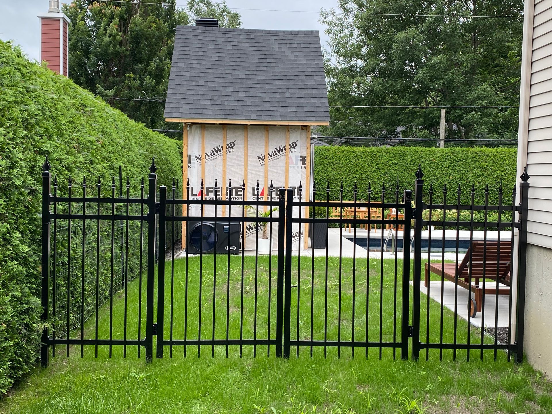 Une clôture en métal noir entoure une cour arrière avec un hangar en arrière-plan.