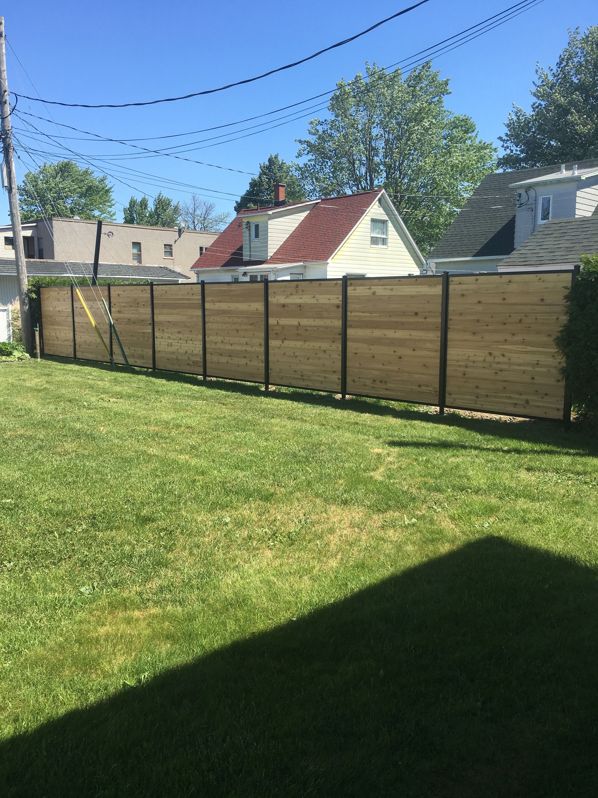 Une clôture en bois entoure une cour verdoyante avec des maisons en arrière-plan.