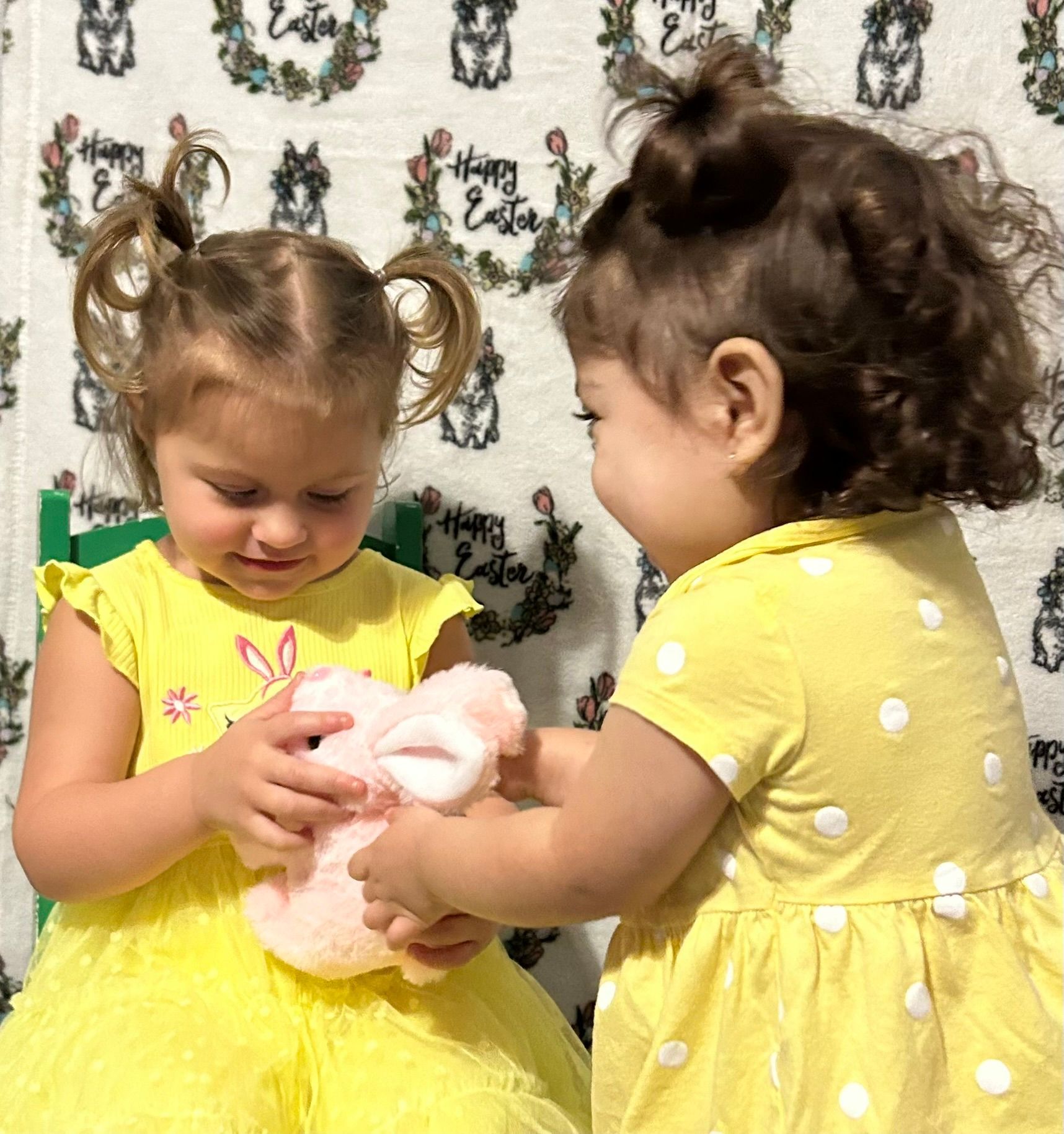 Two toddlers playing with toys in a white salt room. One crouches, reaching for toys. The other sits, also reaching.