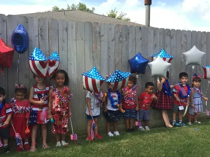 Two children in a playroom with toys. One child smiles, the other looks on. Colorful mats and decor on walls.