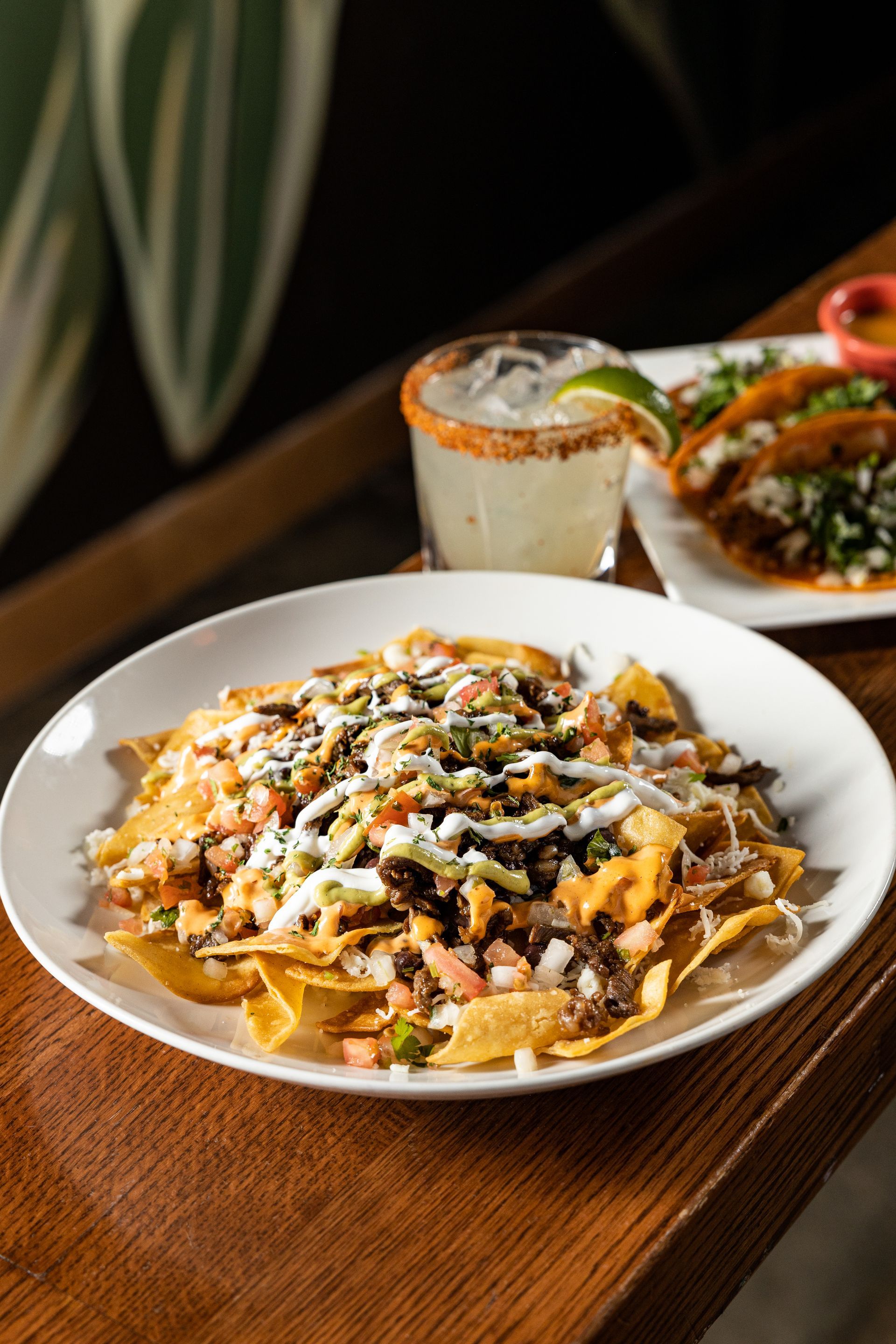 A plate of nachos and a margarita on a wooden table at con safos in denver colorado near coors field
