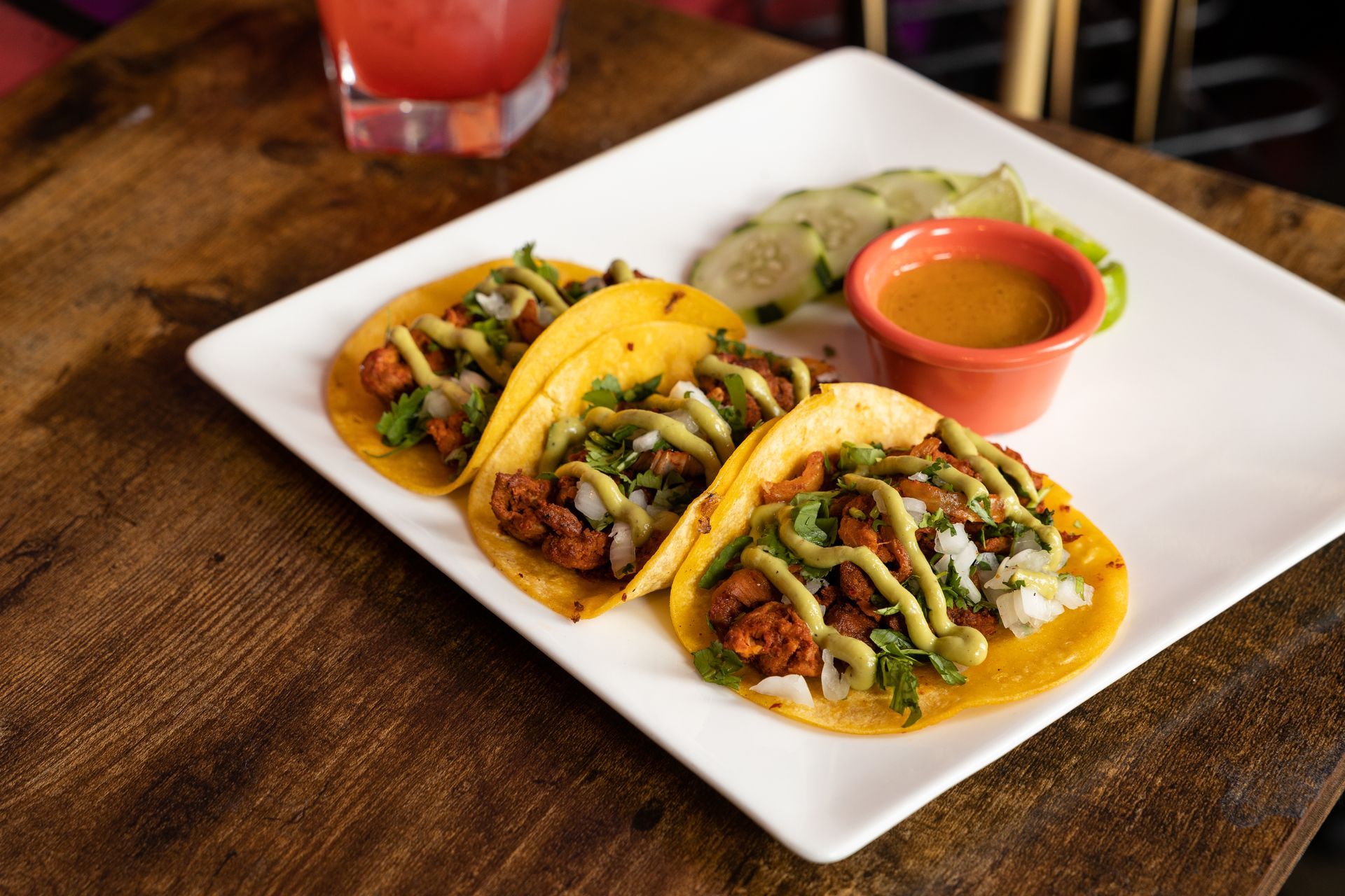 A white plate topped with three tacos and a small bowl of sauce on a wooden table at con safos in denver colorado downtown