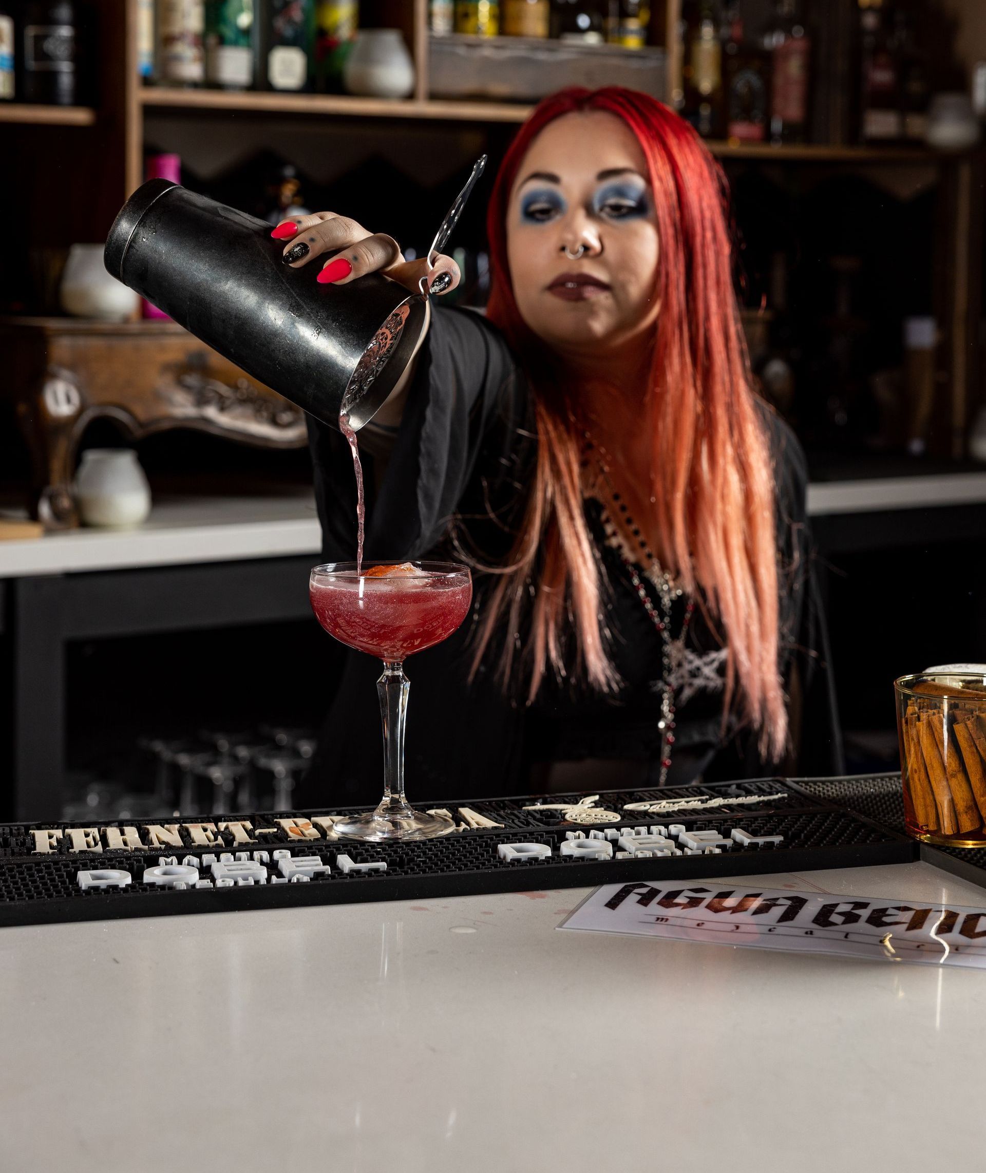 A woman is pouring a drink from a shaker into a glass at agua bendita, a speakeasy in downtown denver colorado