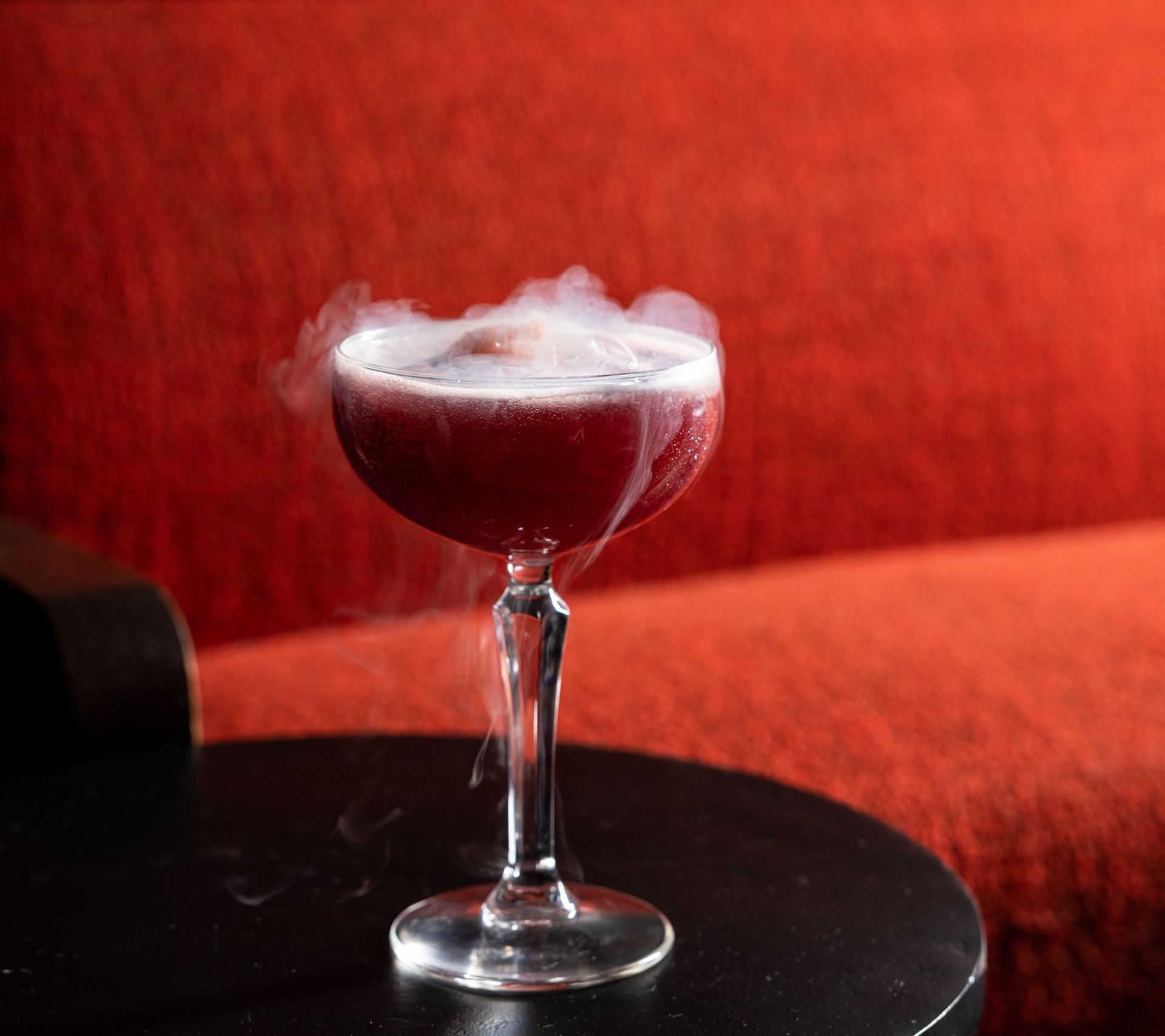 A glass of wine with smoke coming out of it is on a table at agua bendita in denver colorado