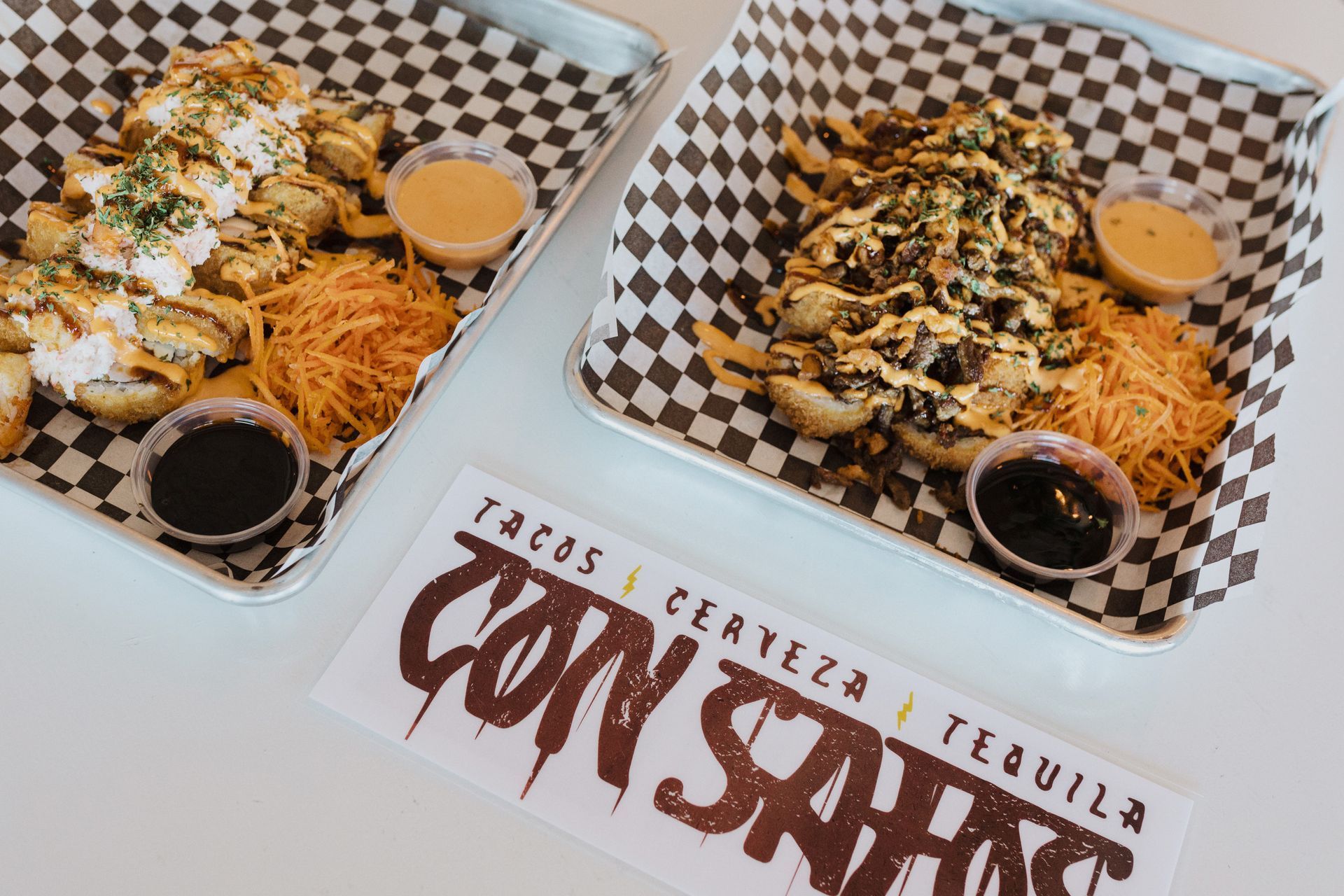 Two trays of food are sitting on a checkered paper on a table at con safos in downtown denver colorado