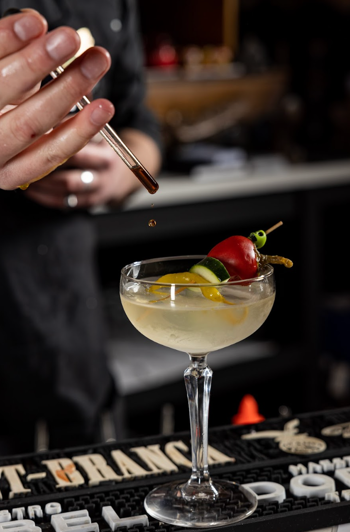 A bartender is pouring a drink into a martini glass at agua bendita in denver colorado