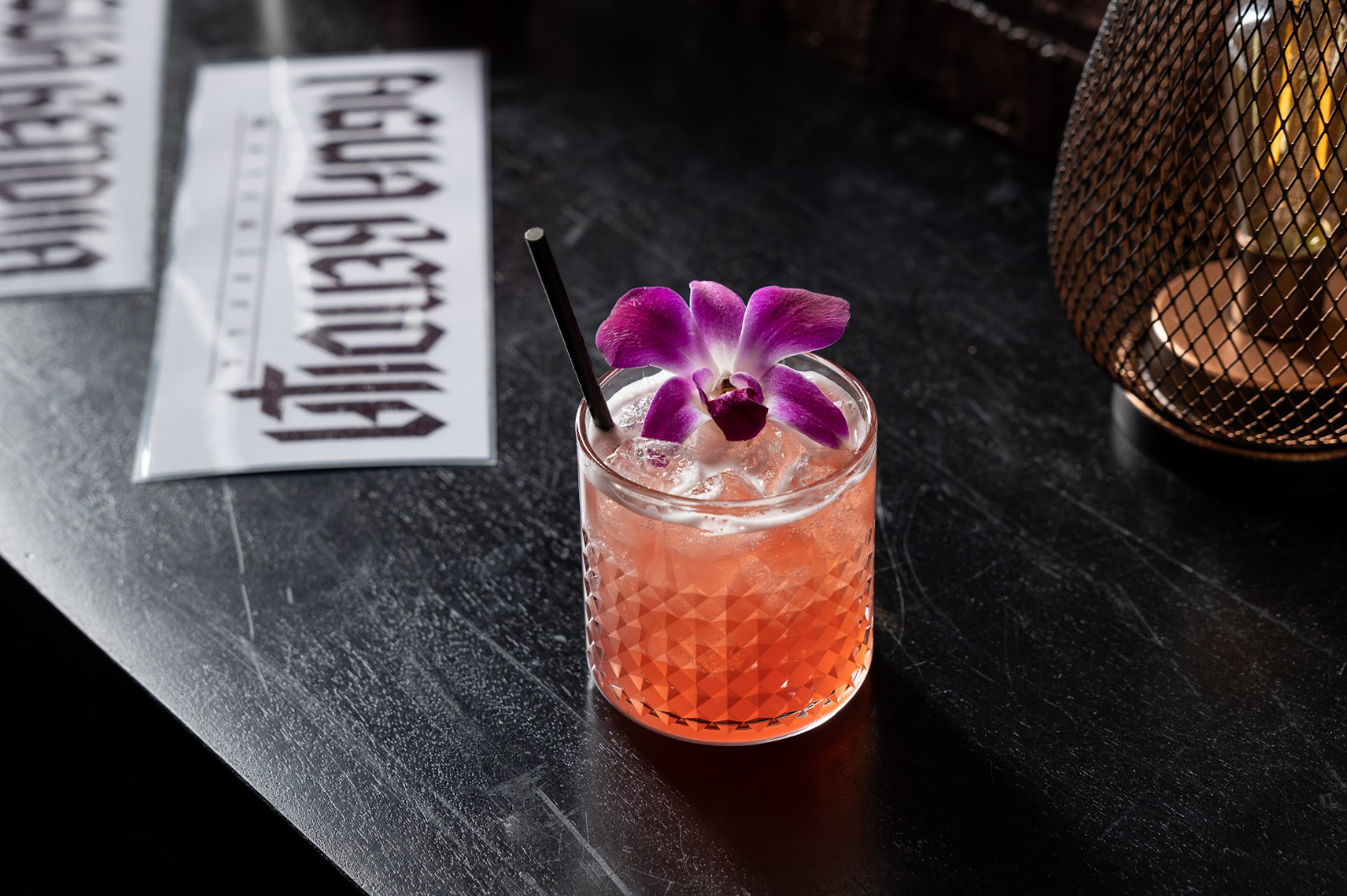 A drink with a purple flower on top of it is on a table at agua bendita in denver colorado