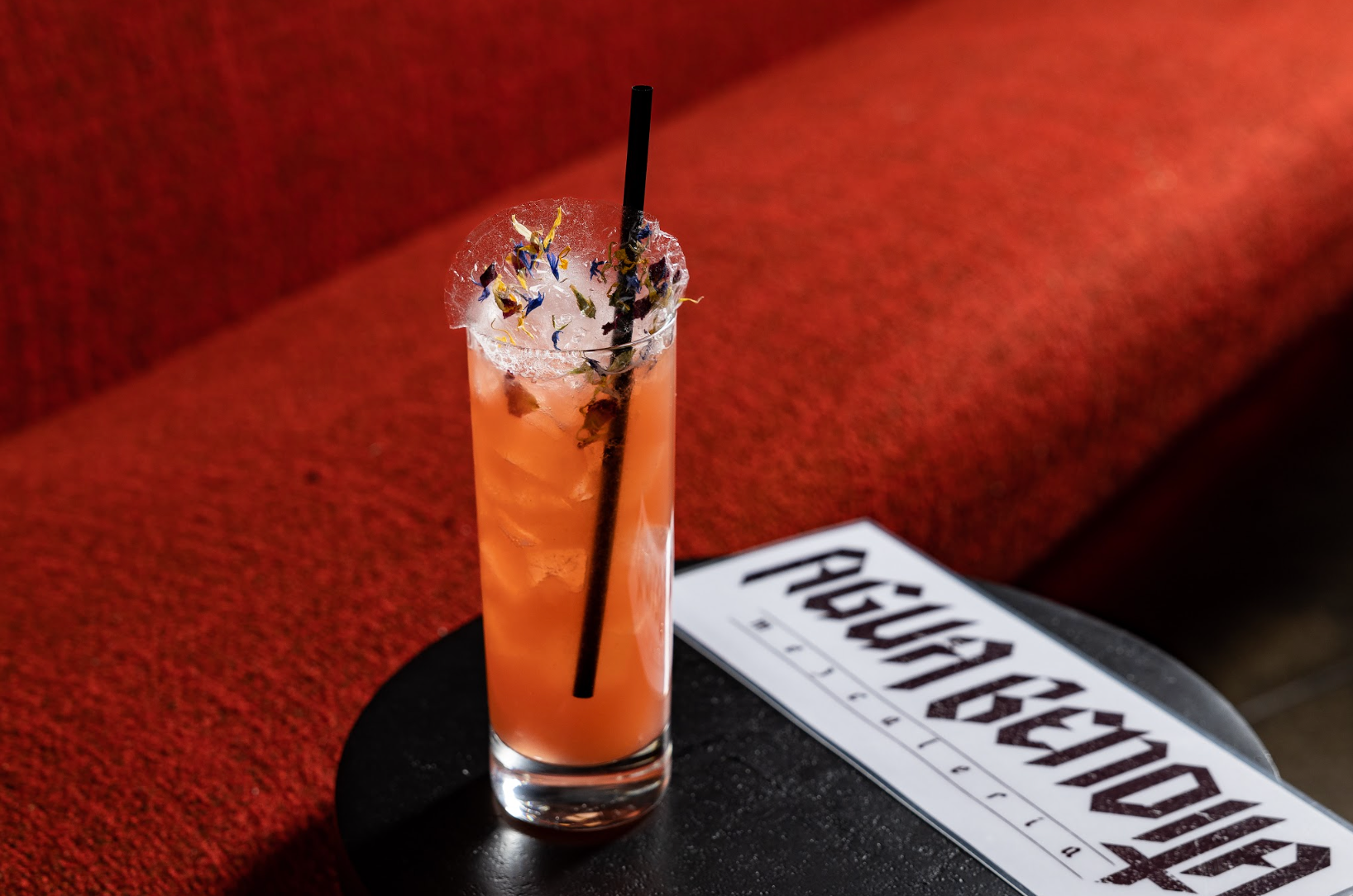A tall glass of orange liquid with a straw on a table at agua bendita, a speakeasy in denver colorado