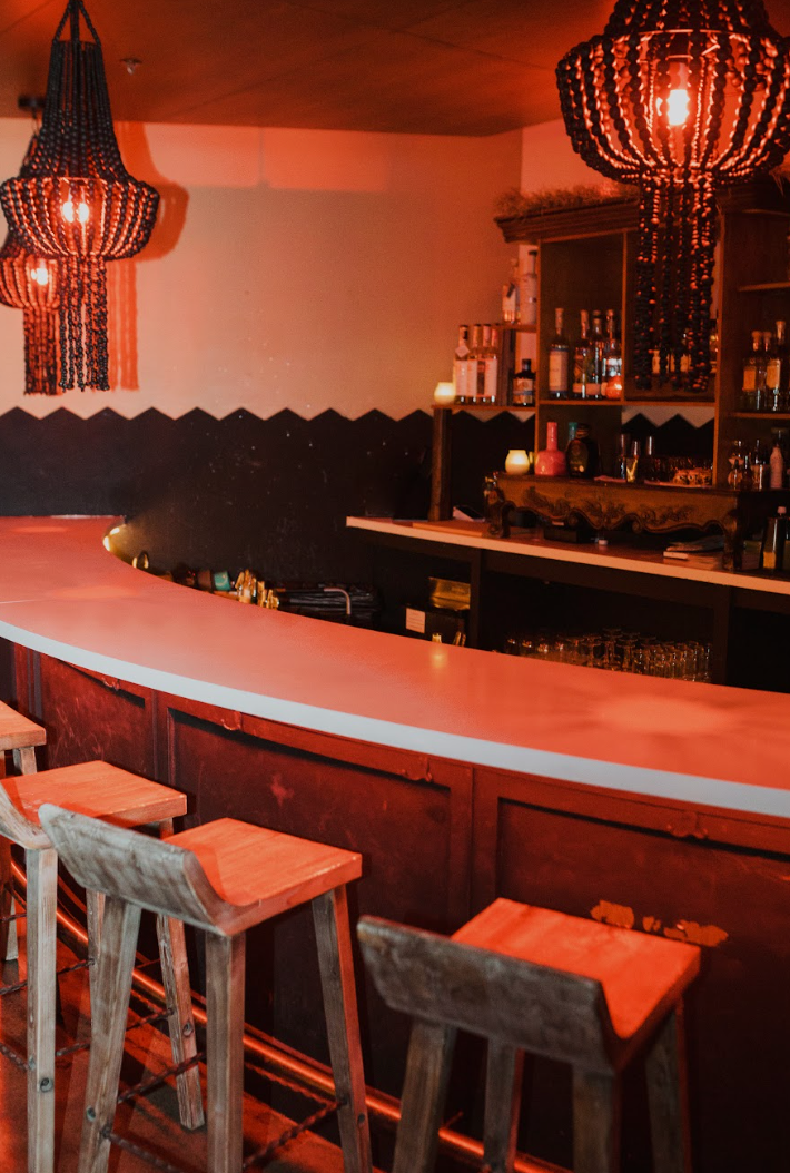 A bar with a long counter and wooden stools at agua bendita, a speakeasy in denver colorado