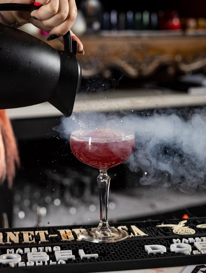 A bartender is pouring a drink into a glass with smoke coming out of it at agua bendita, a speakeasy in denver colorado