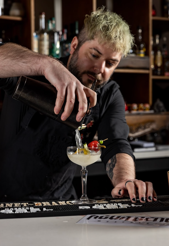 A man is pouring a drink into a martini glass at agua bendita, a speakeasy in denver colorado