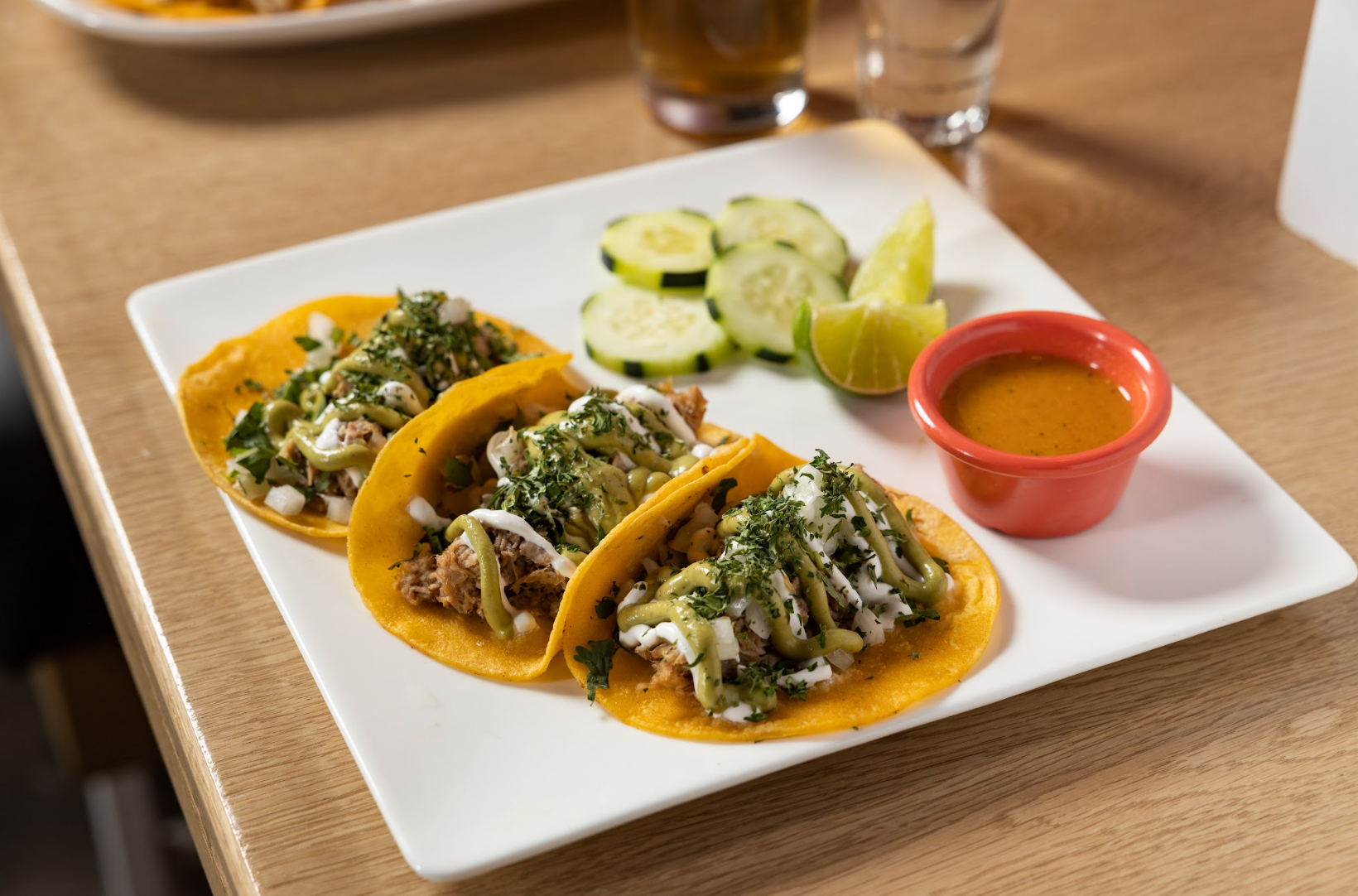 A white plate topped with tacos , cucumbers and salsa on a table at con safos in denver colorado