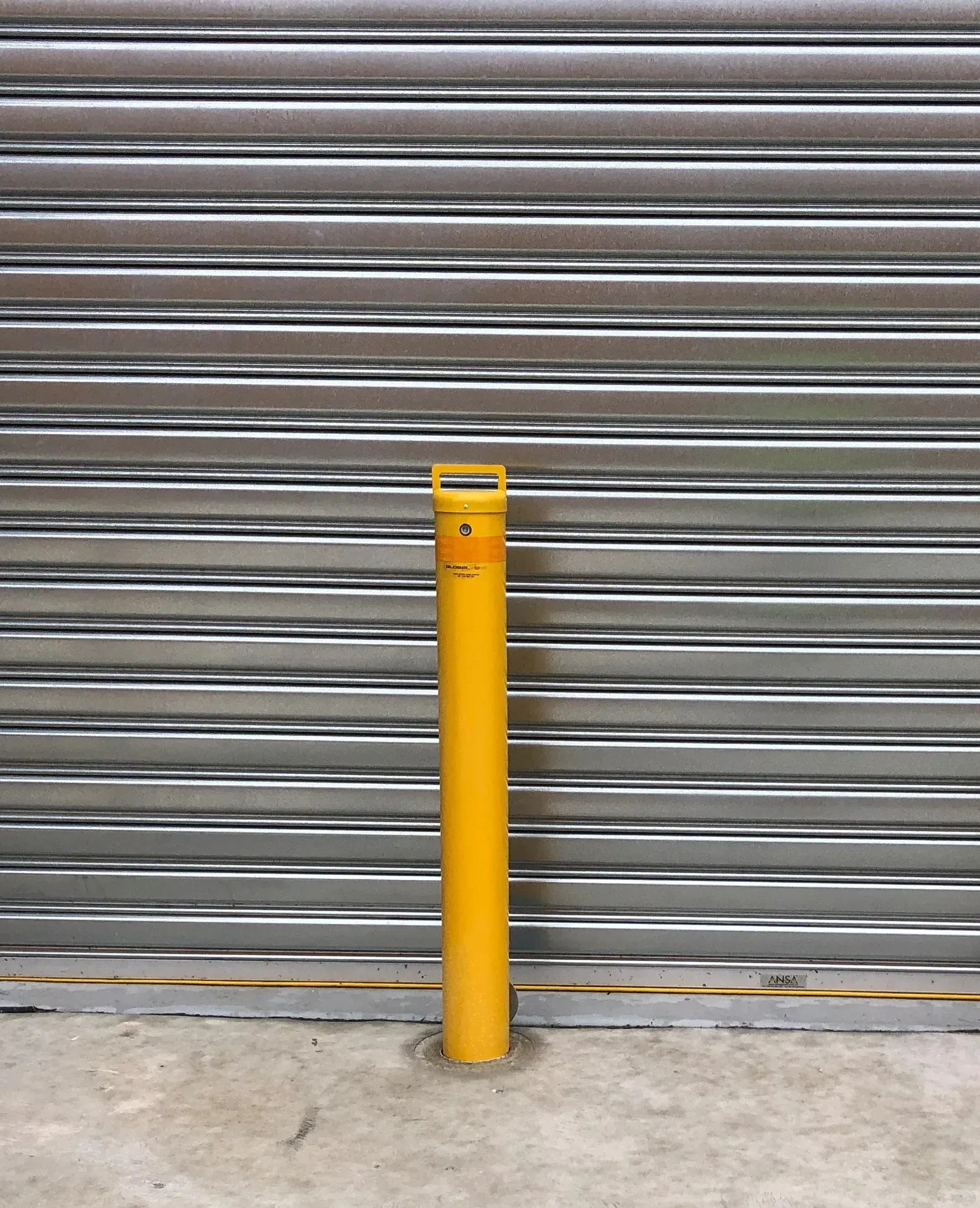 1 yellow bollard in front of a roller door