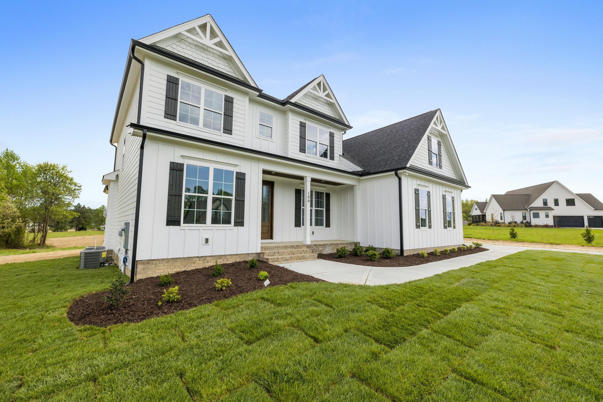 A large white house with black shutters is sitting on top of a lush green field.