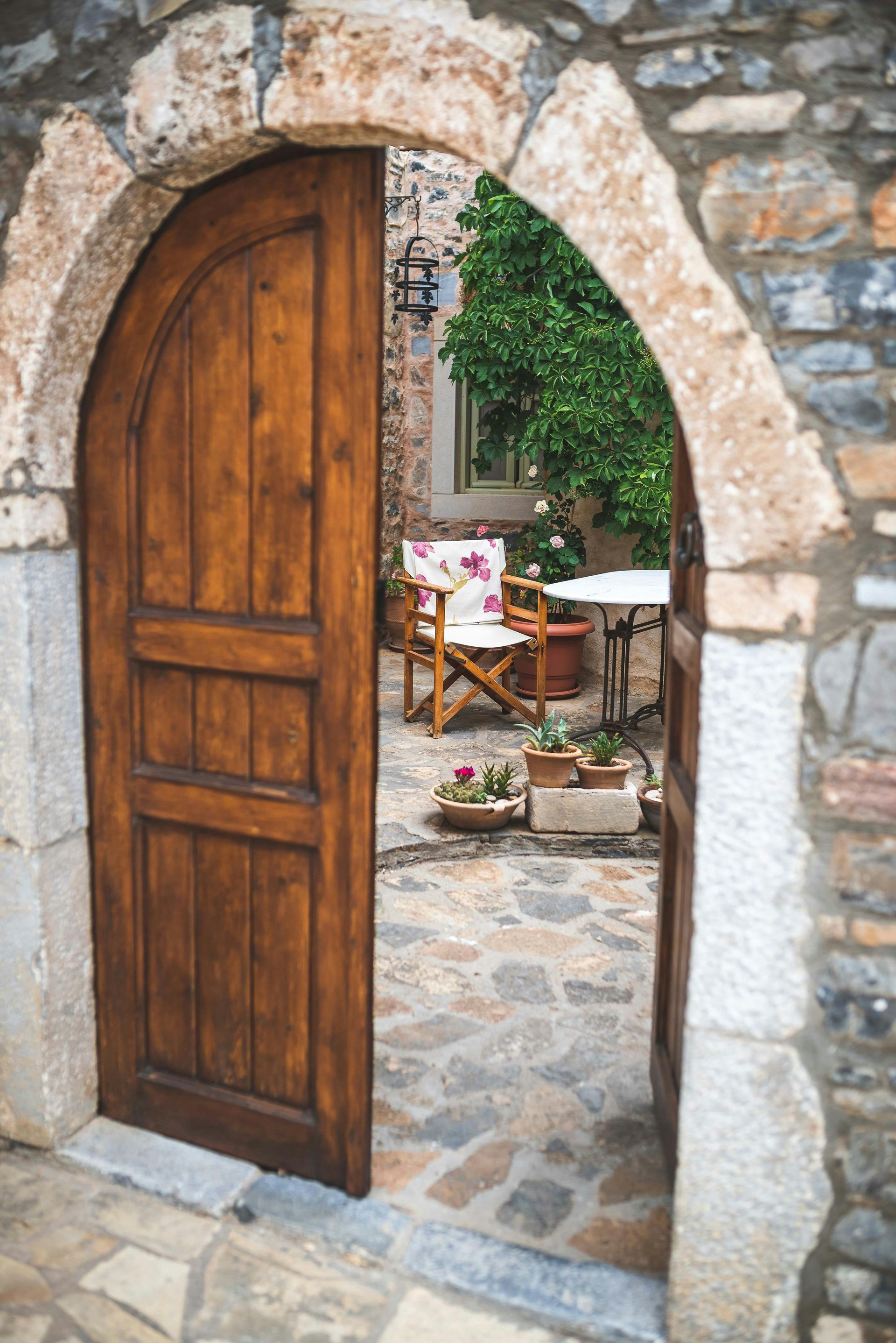 A wooden door is open to a stone archway leading to a patio.