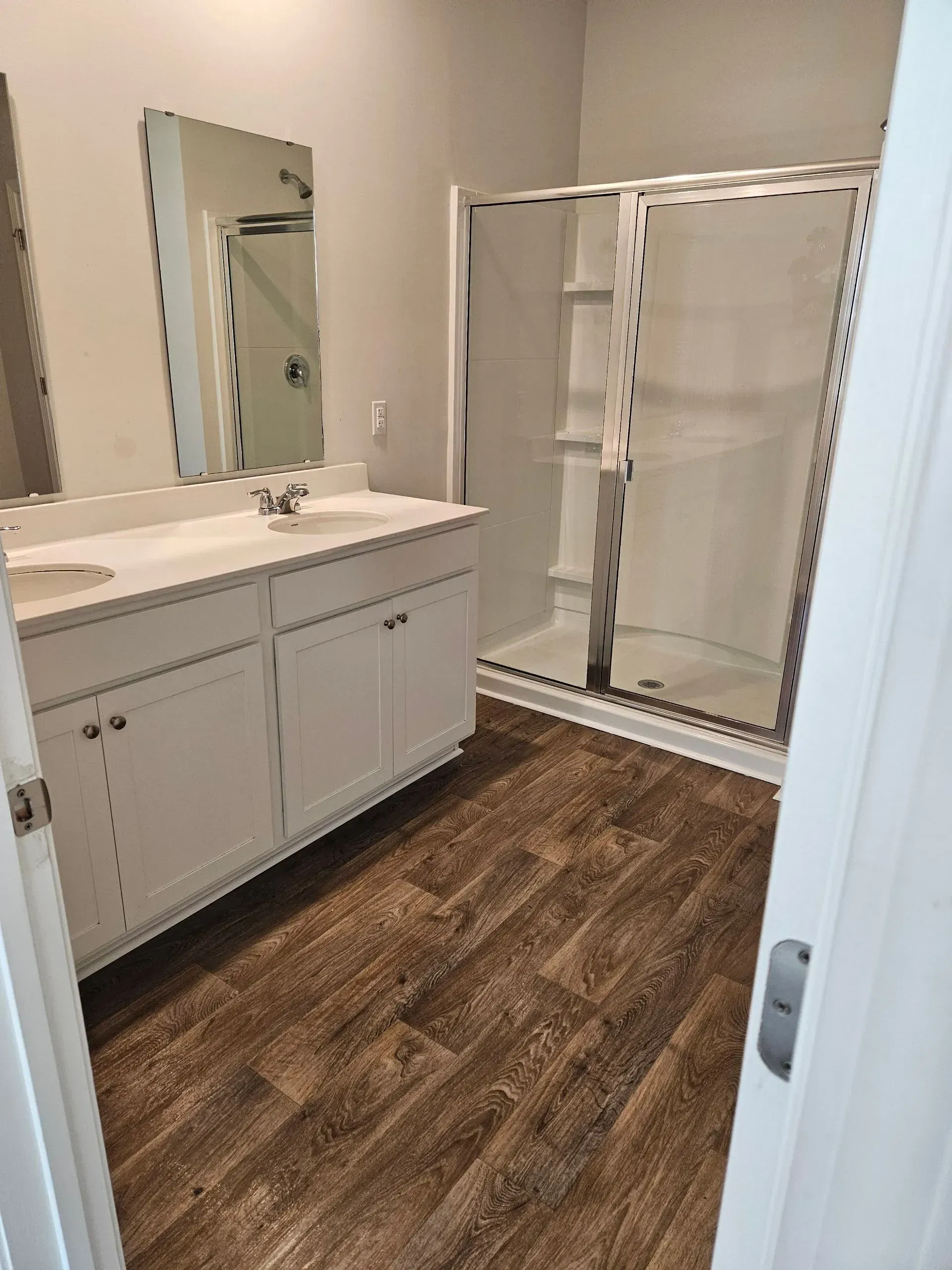 Bathroom with white cabinets, a glass shower, and wood-look flooring.