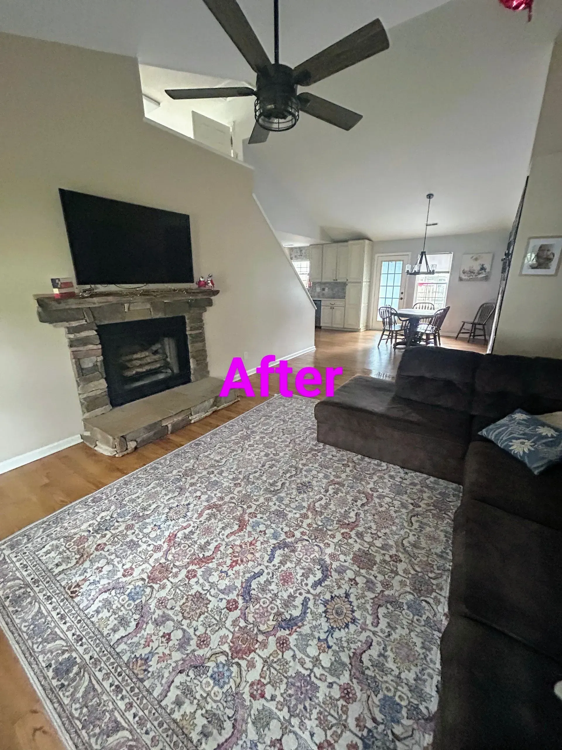 Living room with fireplace, TV, and rug; neutral walls, brown sofa, view of kitchen and dining area.