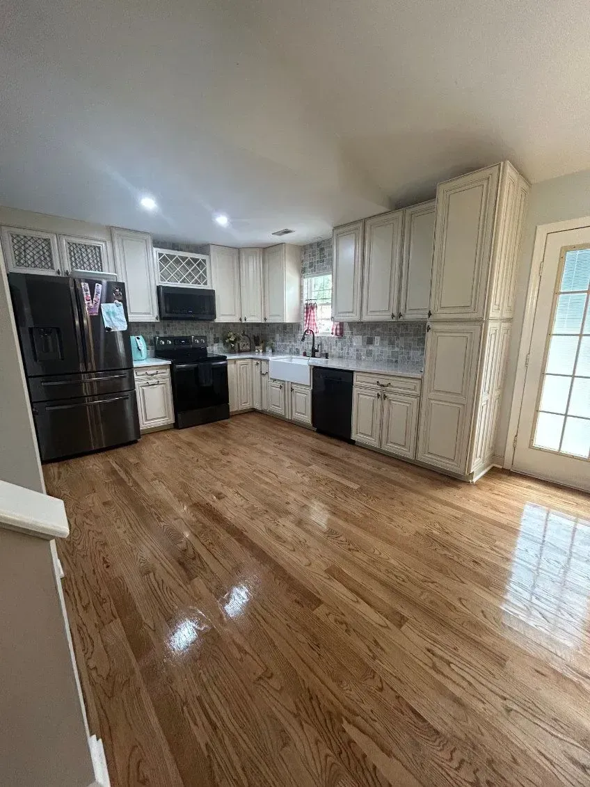 Kitchen with cream cabinets, black appliances, wood floor. Bright, natural light.