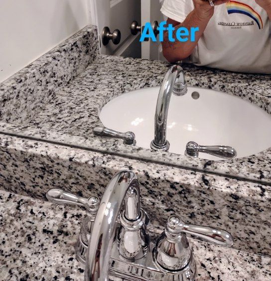 Bathroom vanity with a granite countertop, white sink, and chrome faucet. Person in white shirt reflects in the mirror.