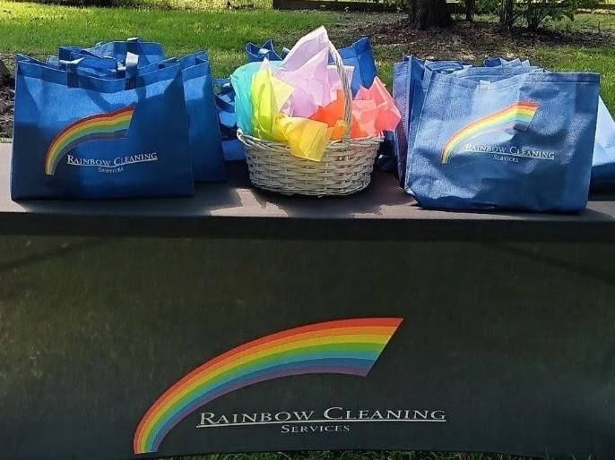Blue tote bags and a basket with rainbow flags on a bench; the Rainbow Cleaning Services logo is visible.