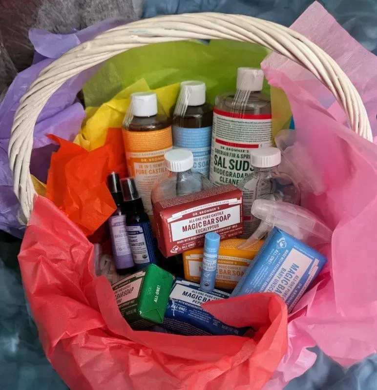 Basket filled with various soaps and cleaning products, arranged with colorful tissue paper.