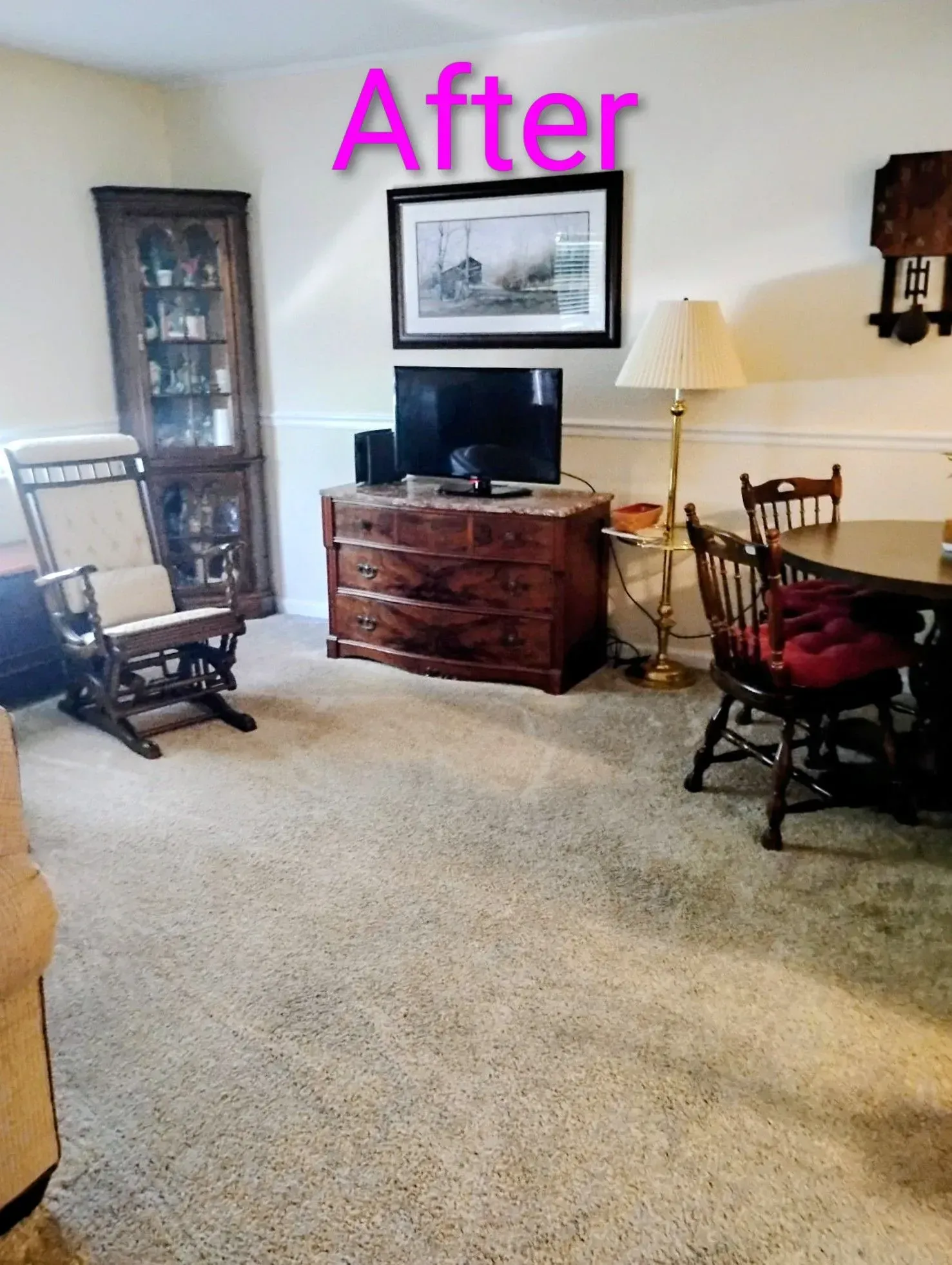 Living room with a wooden cabinet, TV, rocking chair, and a dining table. Light brown carpet and off-white walls.
