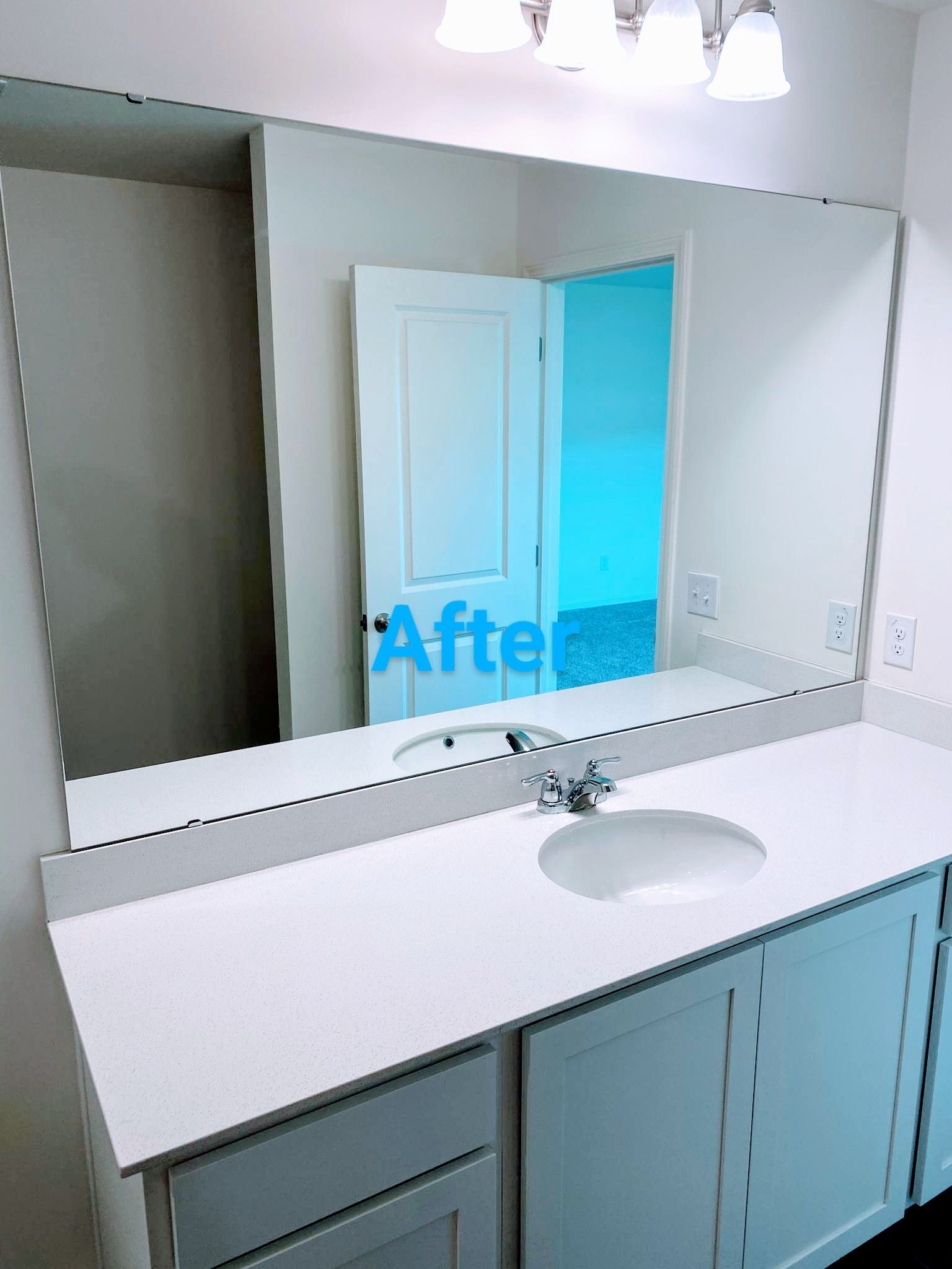 Bathroom vanity with a large mirror, sink, and white countertop. The door is reflected in the mirror.