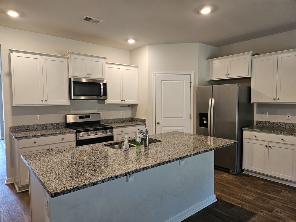 A kitchen with granite counter tops , stainless steel appliances , and white cabinets.