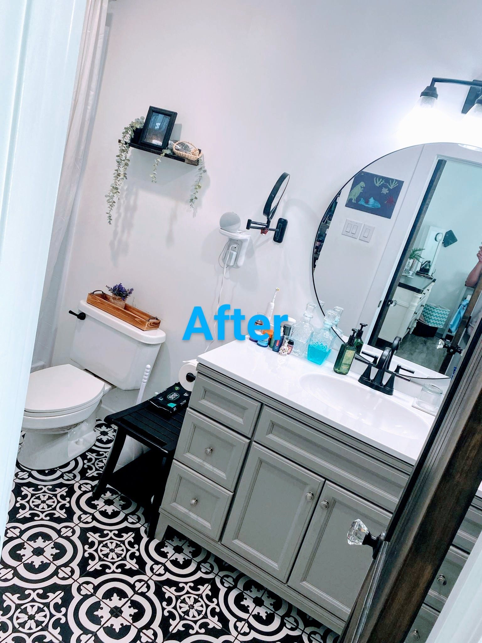 A modern bathroom remodel with black and white patterned floor, grey vanity, and round mirror.