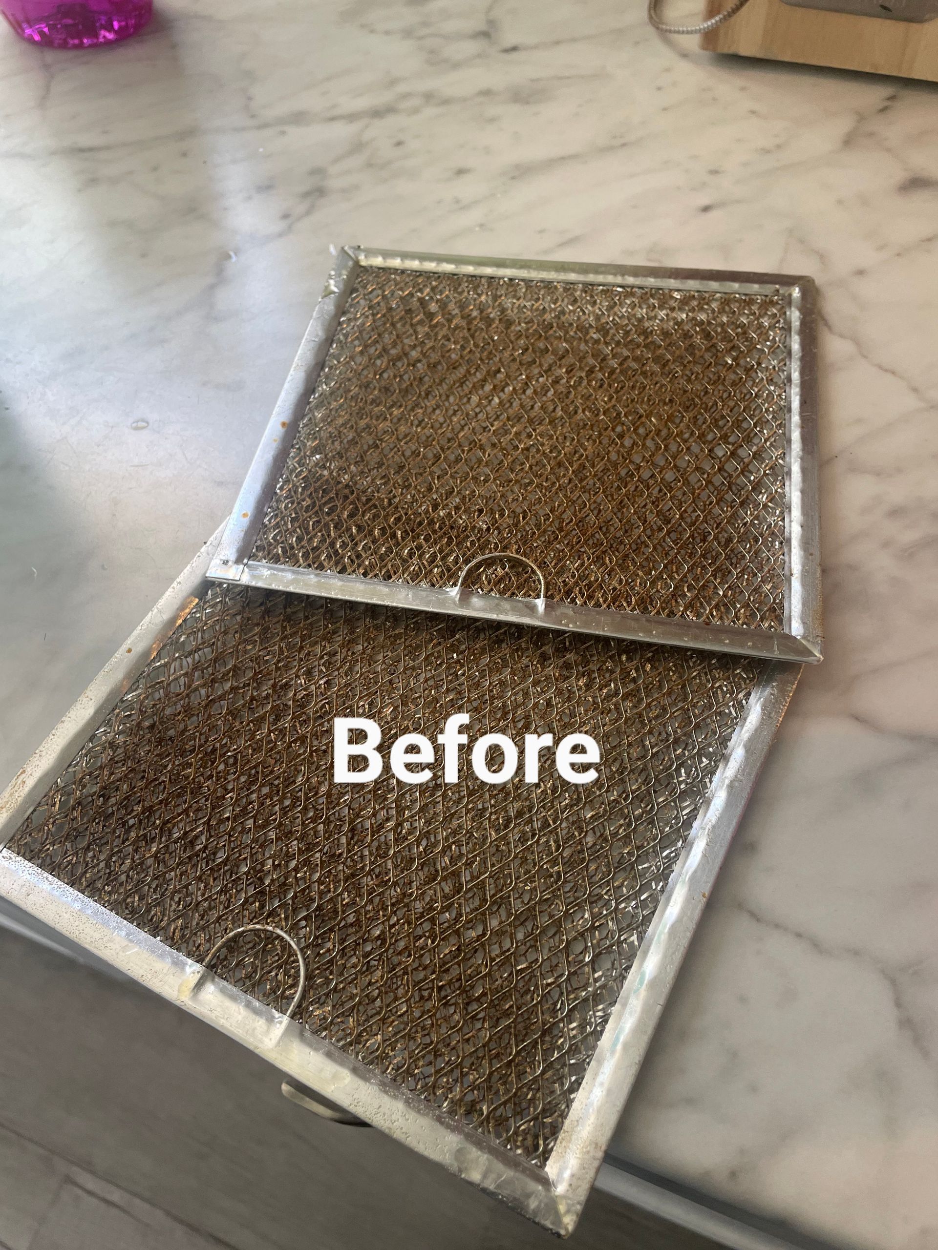 Two dirty, rectangular range hood filters on a countertop, labeled 