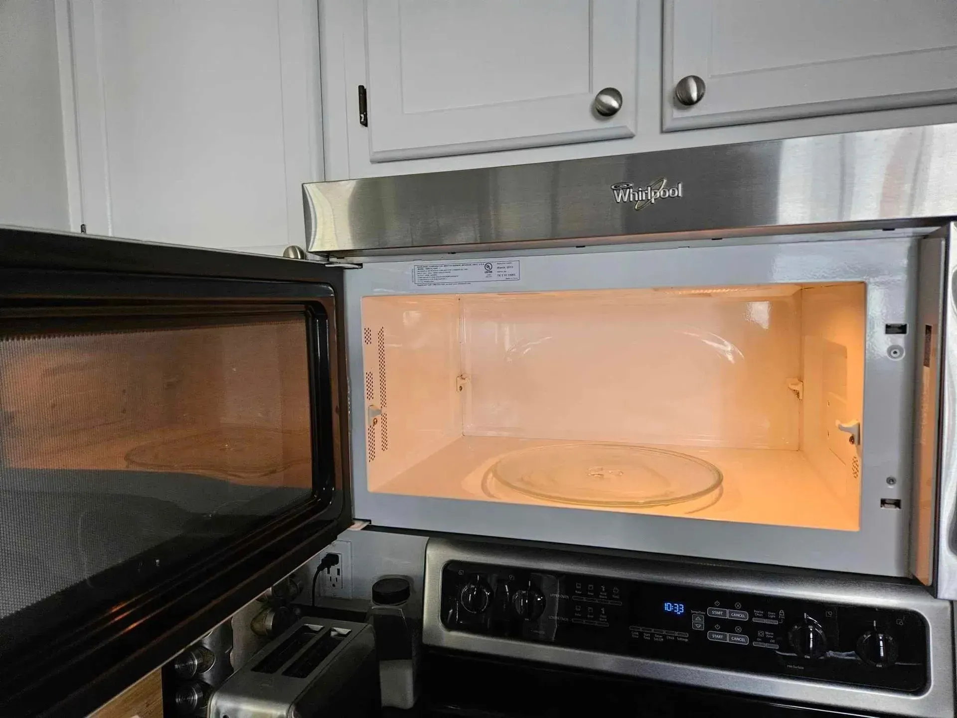 Microwave oven with open door; glass plate inside. Brightly lit interior, built-in above stove.