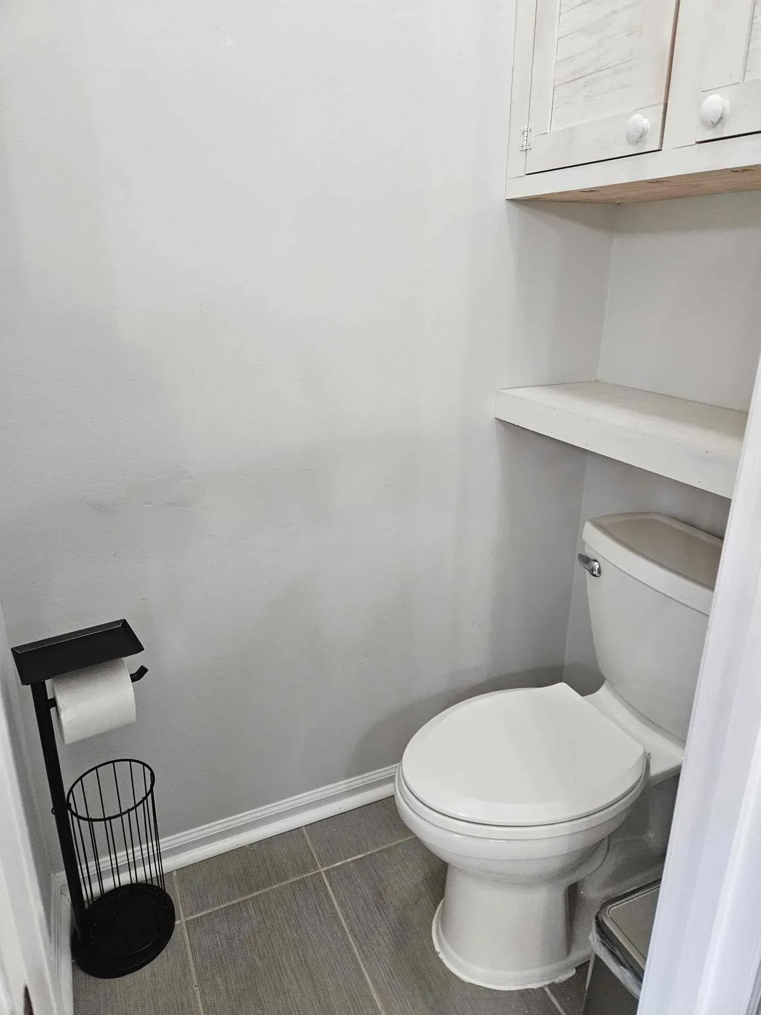 Small bathroom with toilet, cabinet, and toilet paper holder. Gray walls and tile floor.