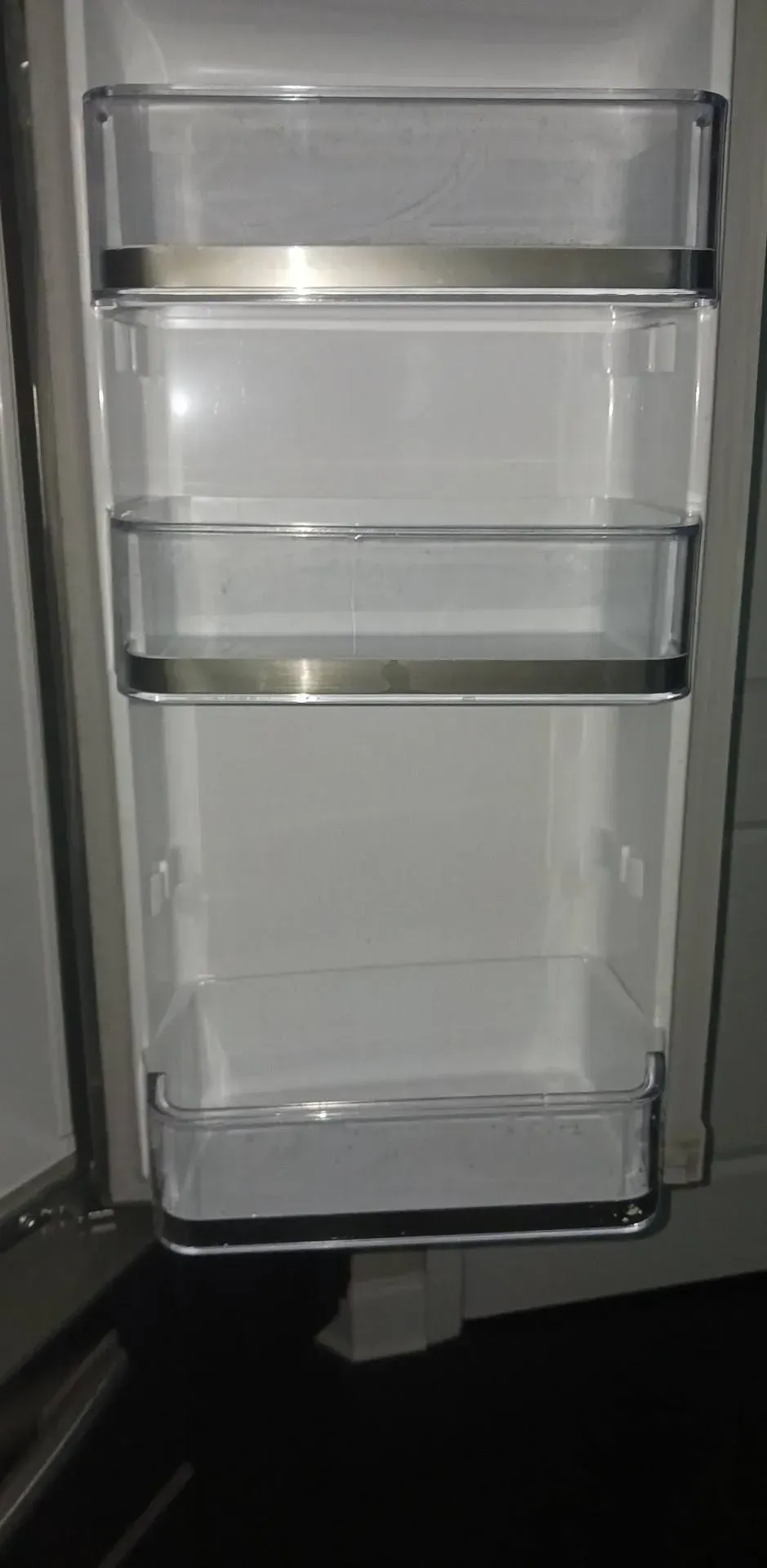 Empty refrigerator door with clear shelves and stainless steel accents.